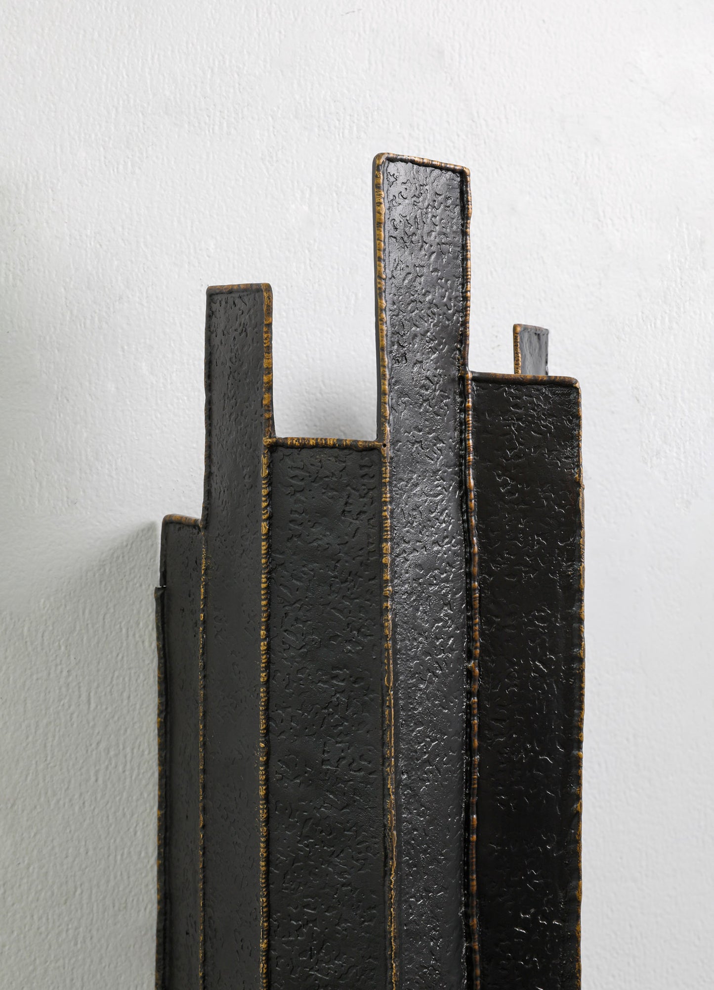 Abstract metal sculpture with a textured black finish and gold accents, featuring tall, rectangular, and irregularly shaped panels arranged vertically against a plain white background.