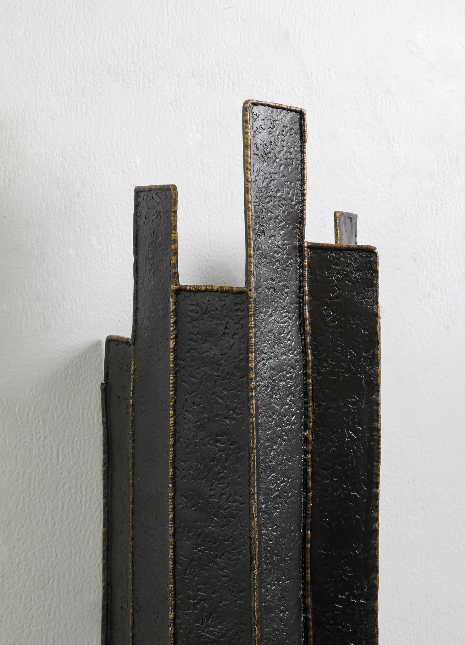 Abstract metal sculpture with a textured black finish and gold accents, featuring tall, rectangular, and irregularly shaped panels arranged vertically against a plain white background.