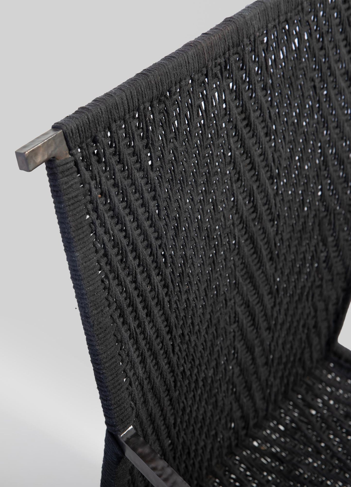 Close-up of a black woven rattan chair back with a metal frame, featuring an intricate pattern and a modern, minimalist design.