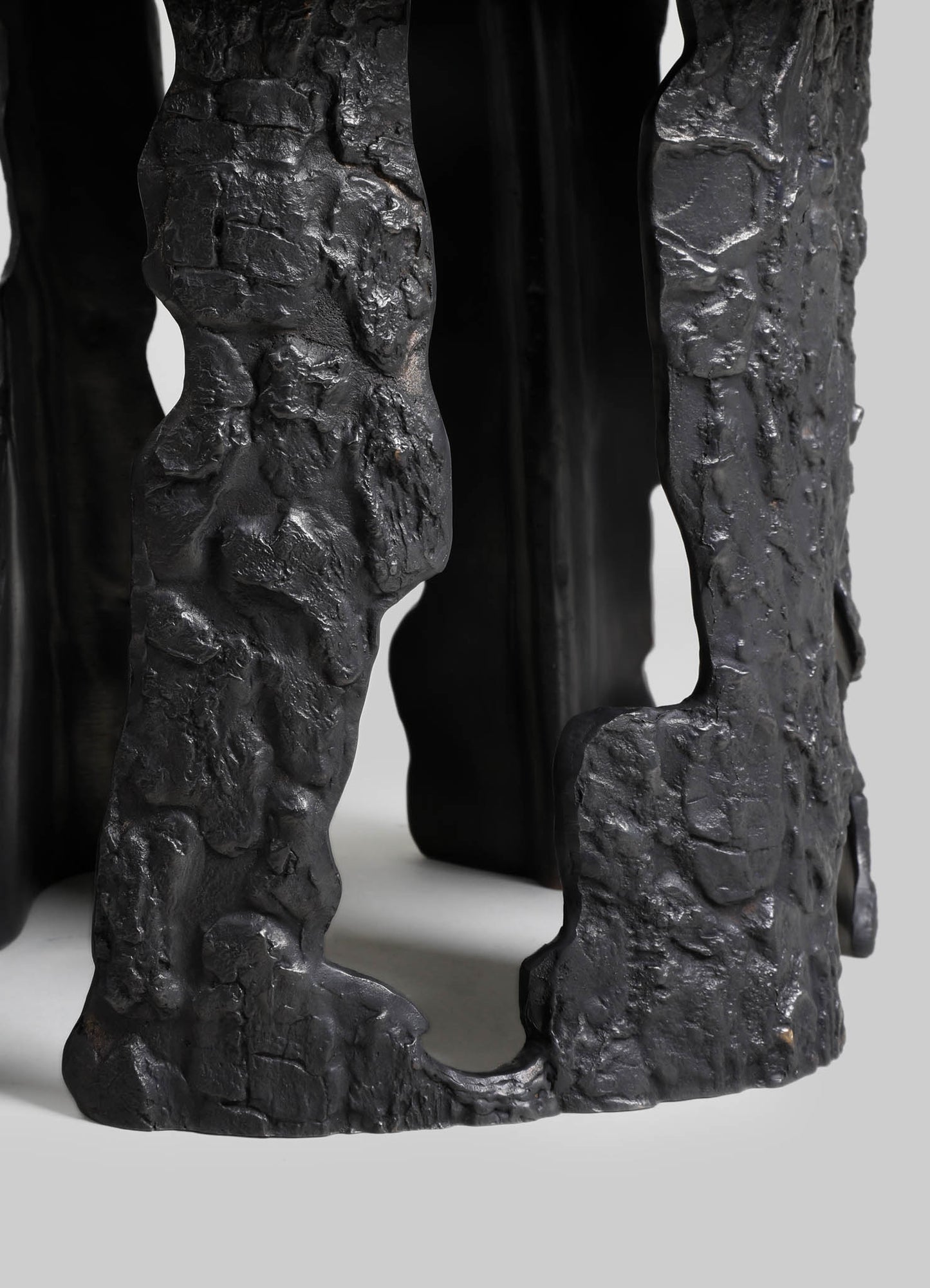 Sculptural black metal table or decorative object with a textured, rough surface and an organic, abstract design, featuring irregular shapes and openings. The piece has a matte finish, emphasizing its handcrafted, rustic style.