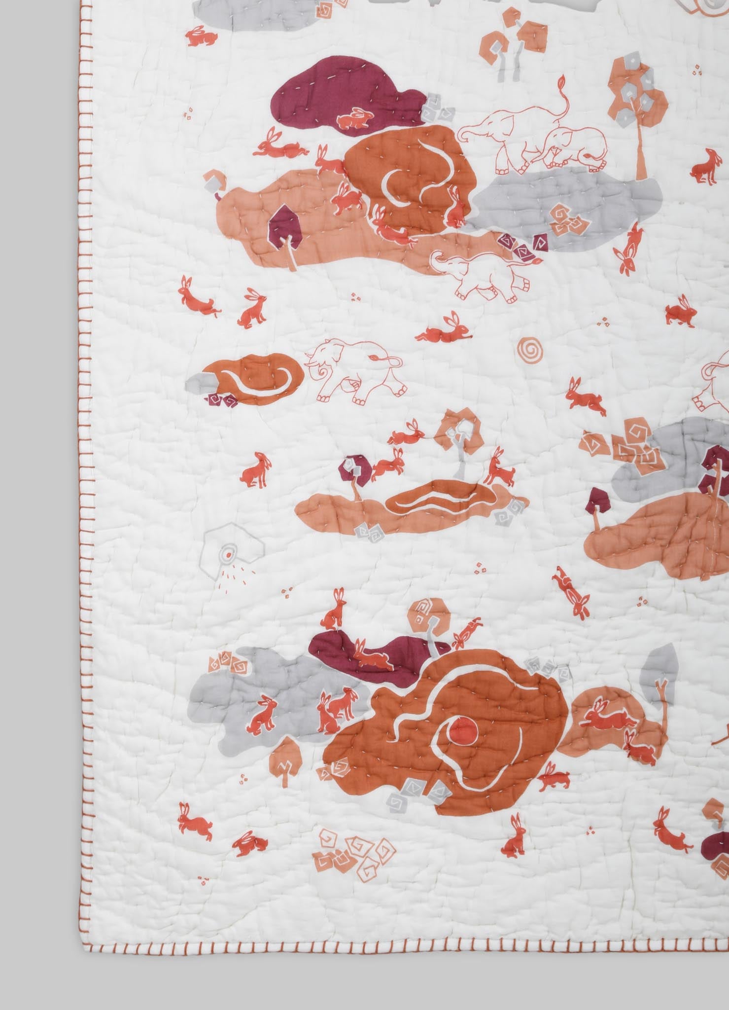 Quilt with embroidered animal motifs, featuring elephants, rabbits, and other creatures, in shades of orange, gray, and maroon on a white background, with a bordered edge.