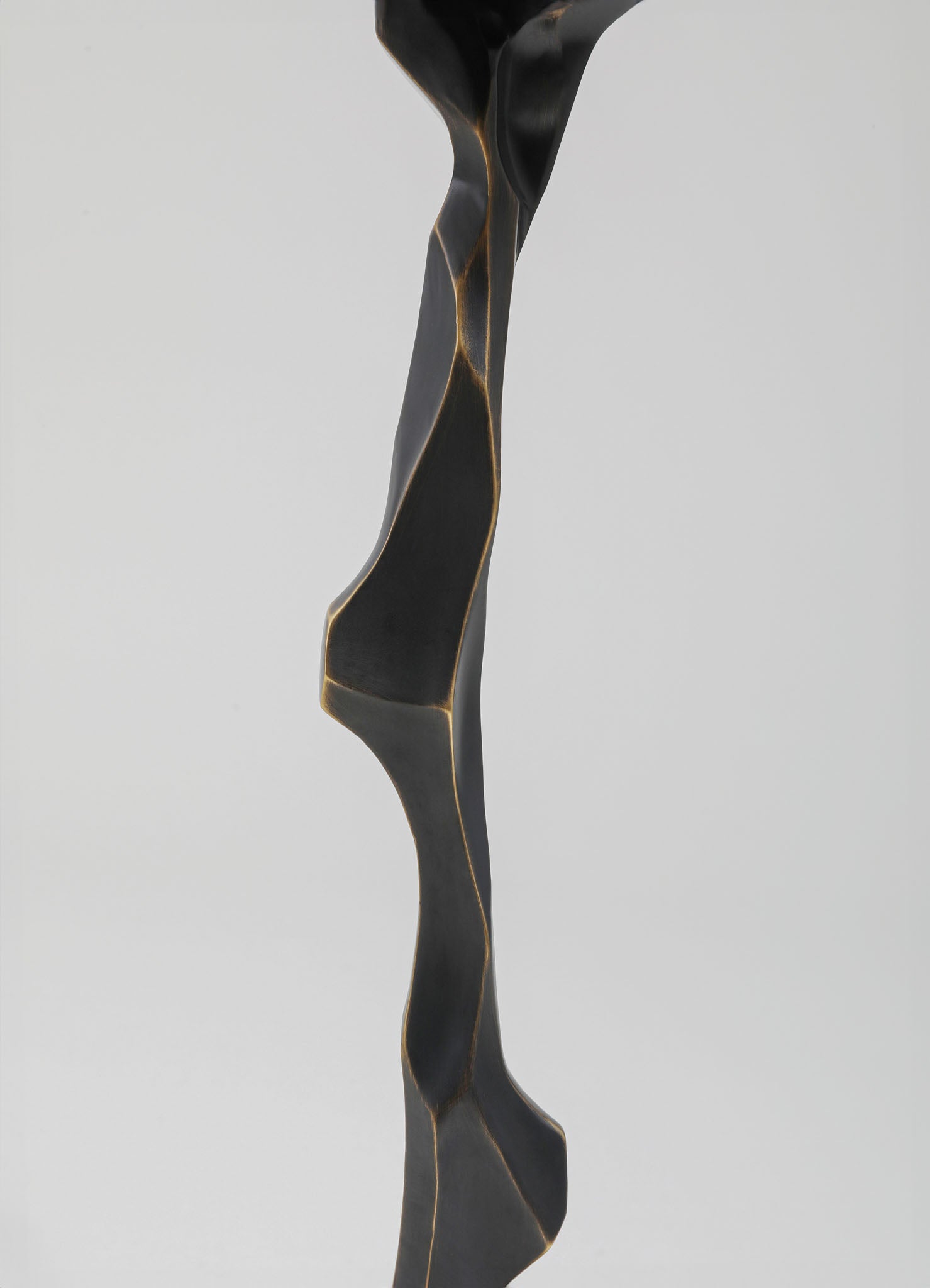 A black sculpture with a twisted, abstract form featuring smooth surfaces and subtle gold veining. The piece has a contemporary and artistic style with an organic, flowing design.