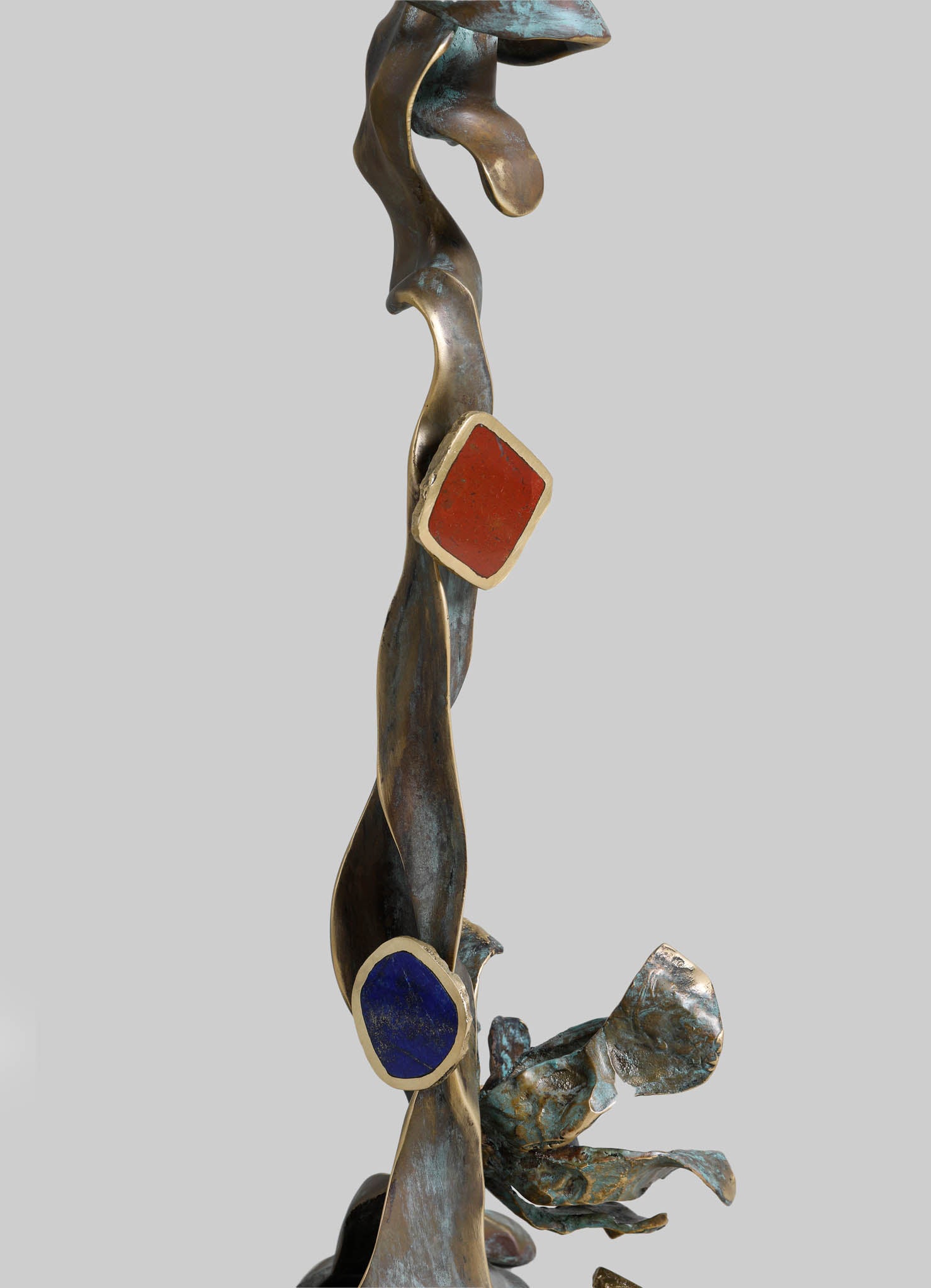 Abstract bronze sculpture with fluid, organic forms and colorful geometric accents in red and blue, set against a neutral background. The artwork features a combination of polished bronze and painted elements, conveying a contemporary and artistic style.