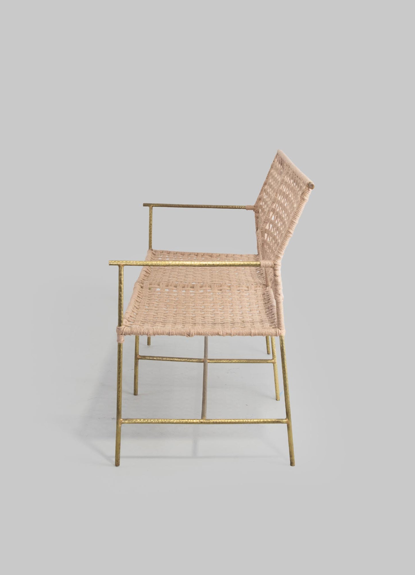 A chair with a metal frame finished in gold and a woven rattan seat and backrest in a light beige color. The design combines contemporary and rustic elements with a simple, elegant silhouette.