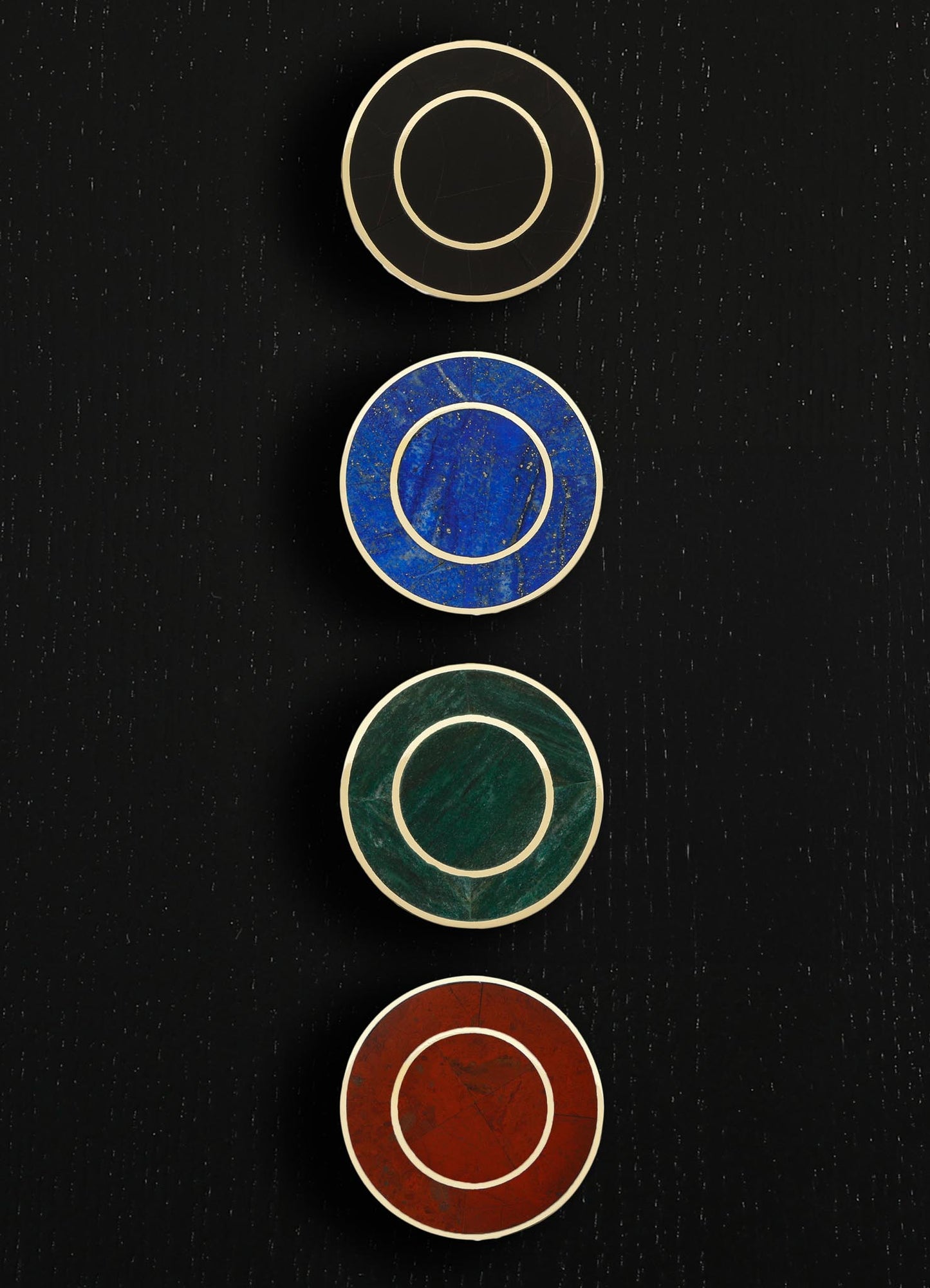 Four round decorative objects with gold-colored borders, featuring textured surfaces in black, blue, green, and red, arranged vertically on a black background.
