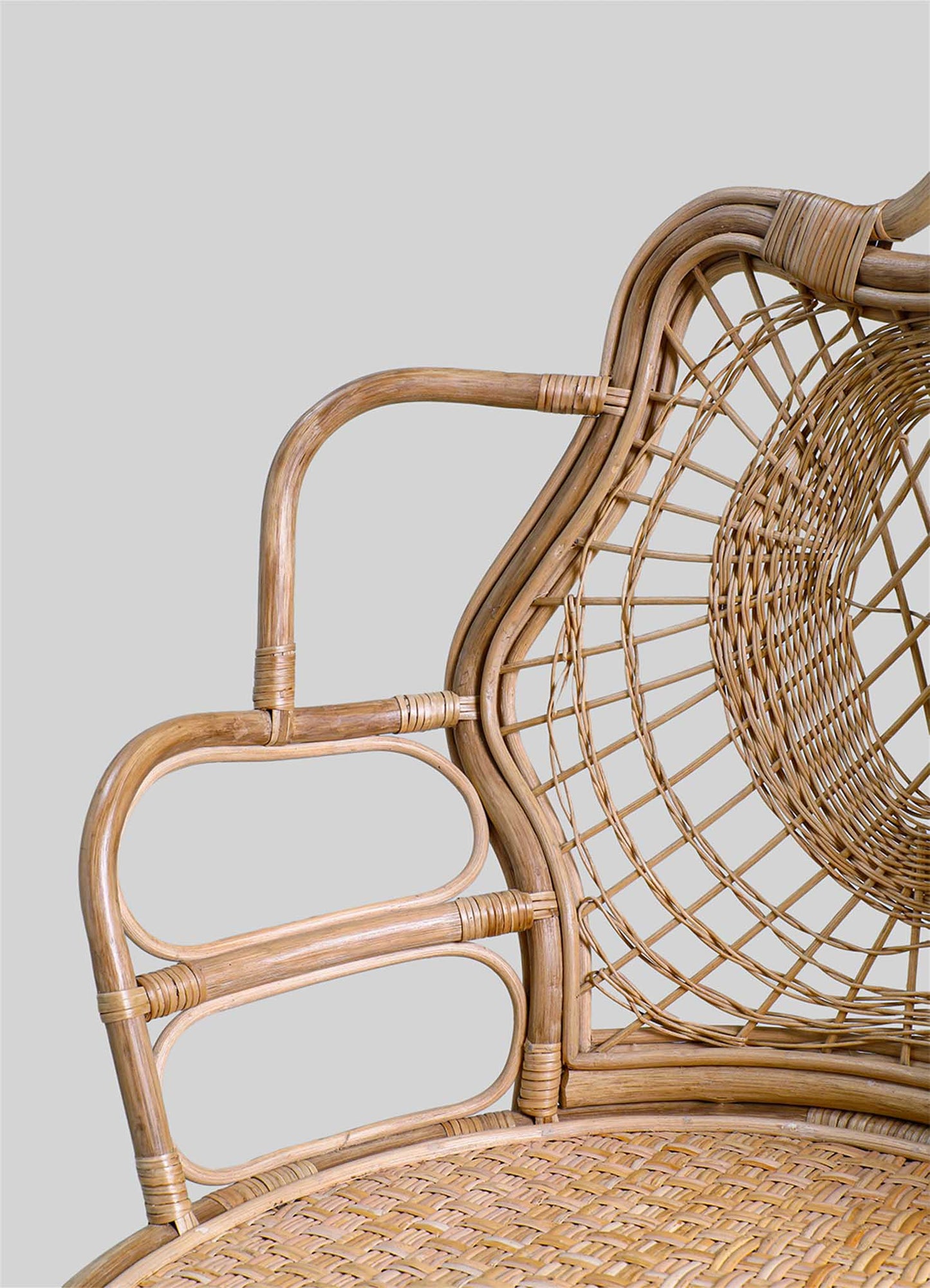 Wicker chair with a rounded backrest and armrests, crafted from natural rattan with a light wood tone. The design features an open, woven pattern on the backrest and seat, emphasizing a handcrafted, rustic style.
