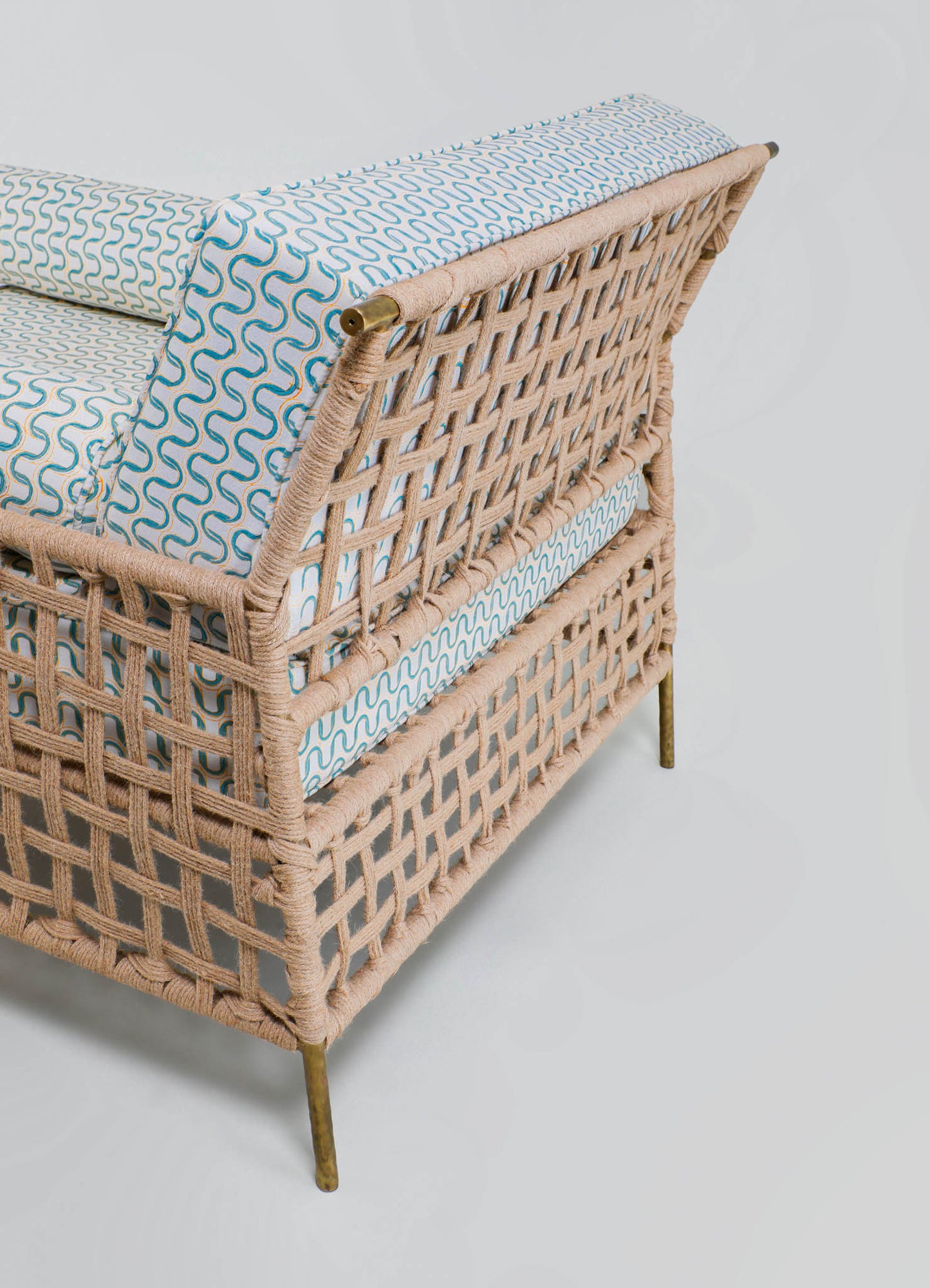 Wicker bed frame with a light natural finish featuring a woven pattern and brass accents on the corner supports, paired with a mattress and bedding in a light blue and white geometric print.