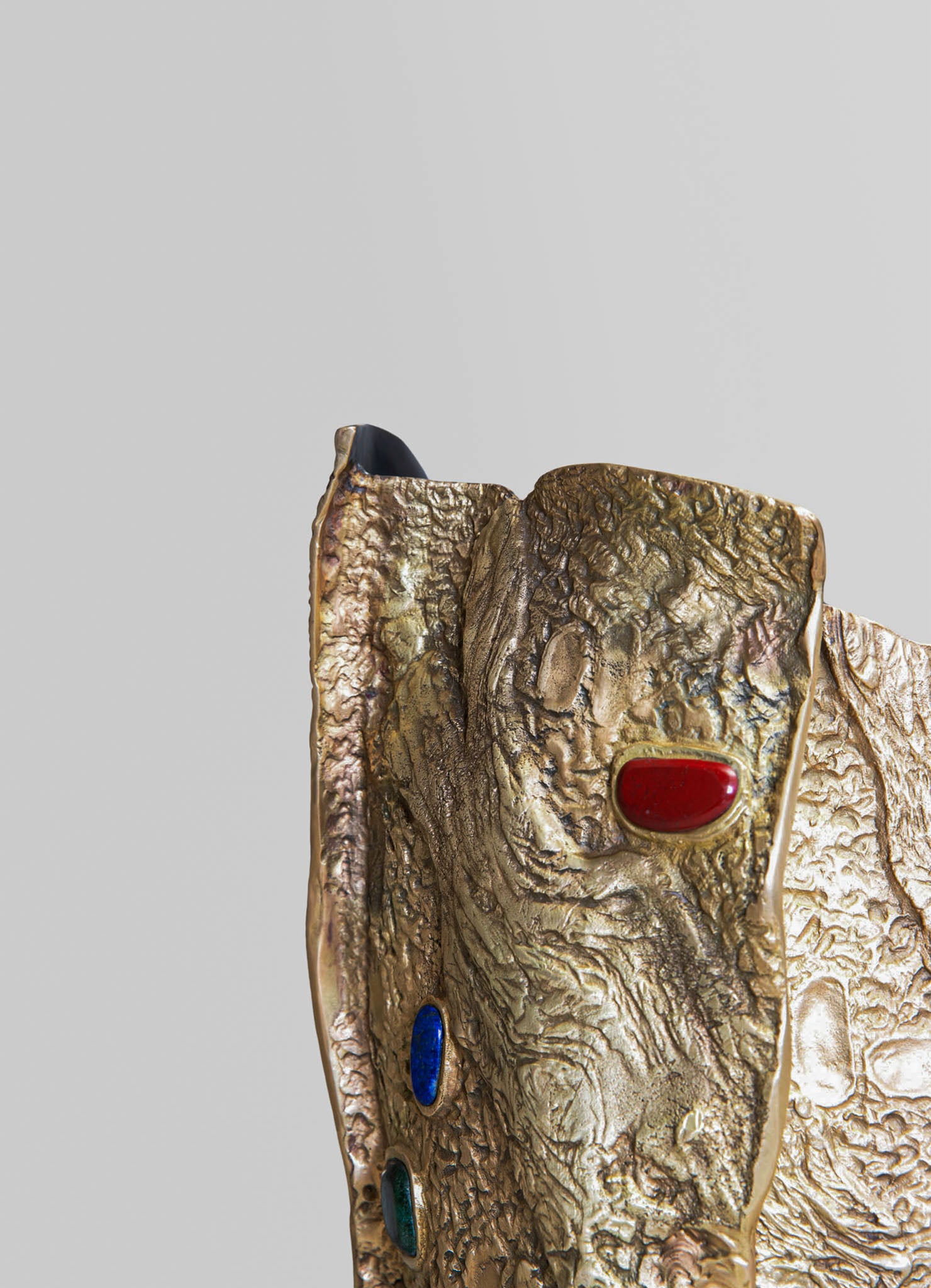 A decorative sculpture with a textured, gold-toned surface and colorful oval accents in red, blue, and green. The piece has an abstract, organic design and a mix of metallic and matte finishes.