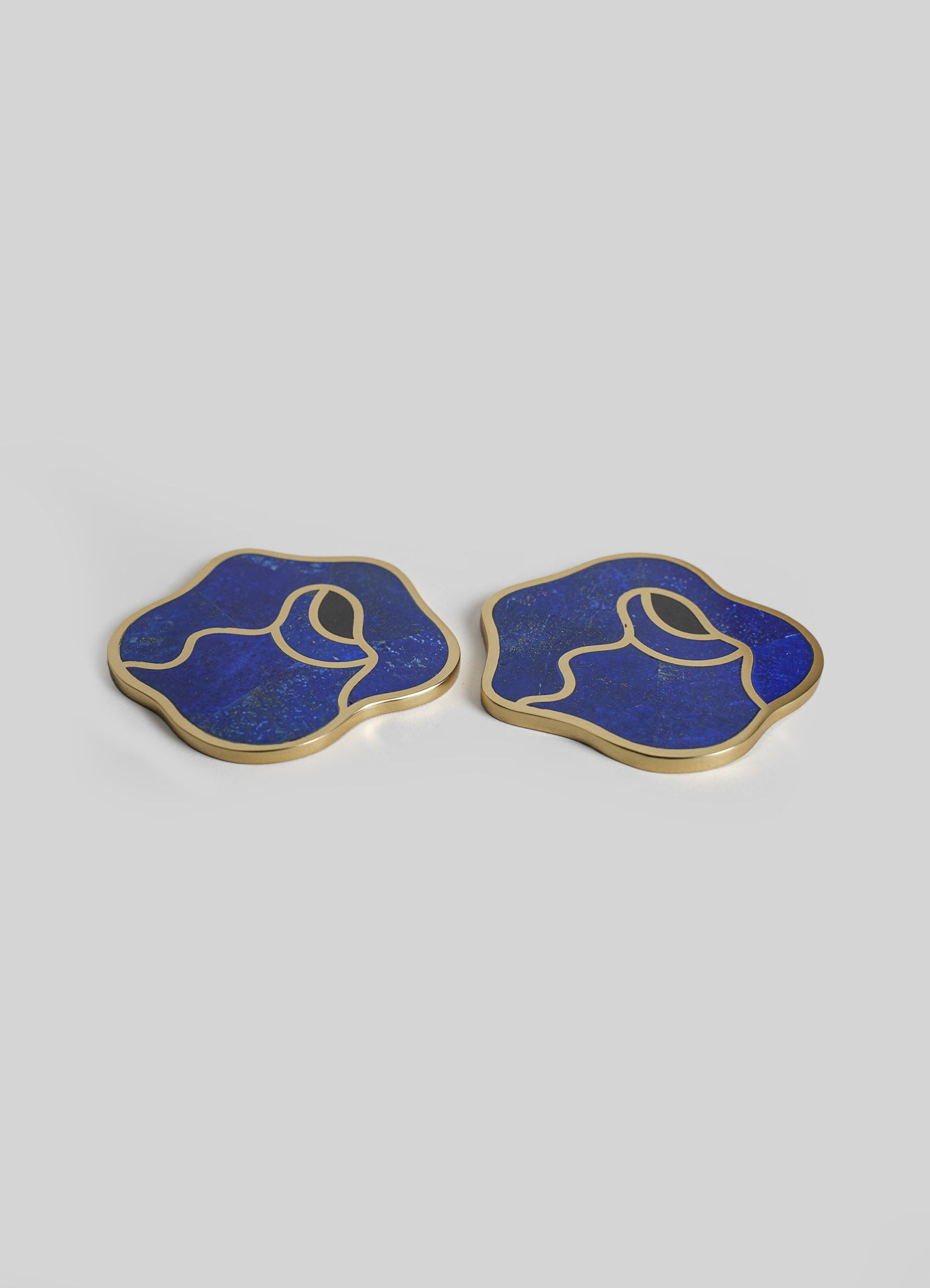 Pair of decorative coasters with irregular, abstract shapes, featuring deep blue resin with gold trim and fine speckled details.
