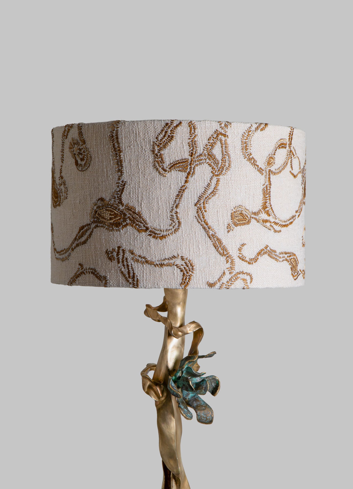 Fabric lampshade with a botanical or floral pattern in beige and brown tones, mounted on a sculptural base resembling a twisted natural branch with a metallic finish.