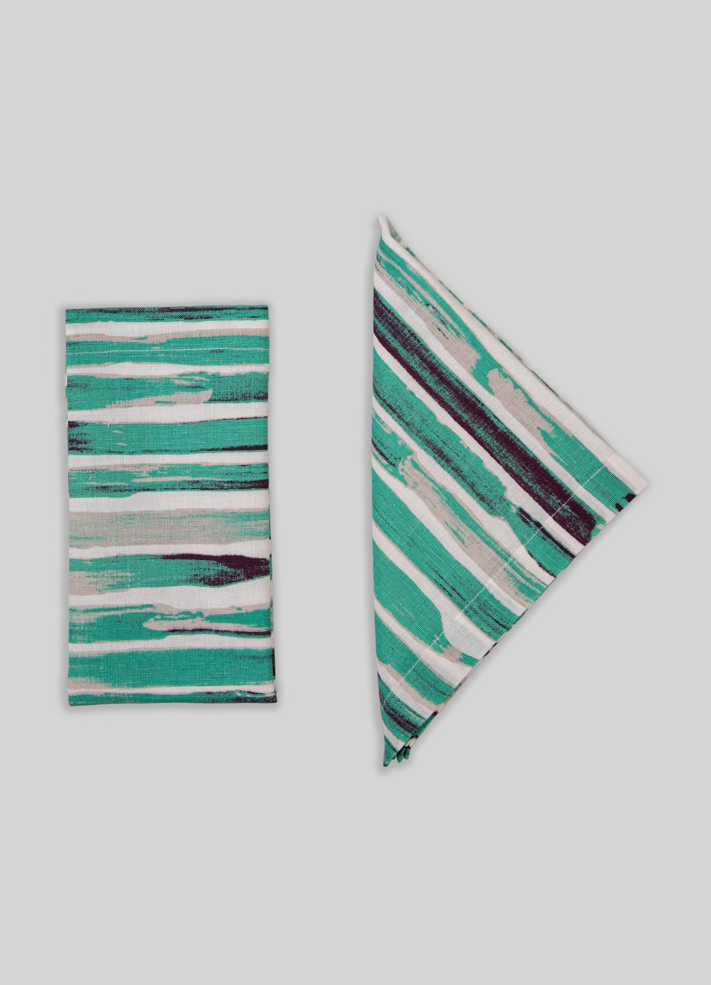 Striped textile accessories with abstract watercolor-like patterns in shades of teal, turquoise, white, and dark purple. The set includes a folded cloth and a napkin or placemat, crafted from woven fabric with a modern, artistic style.