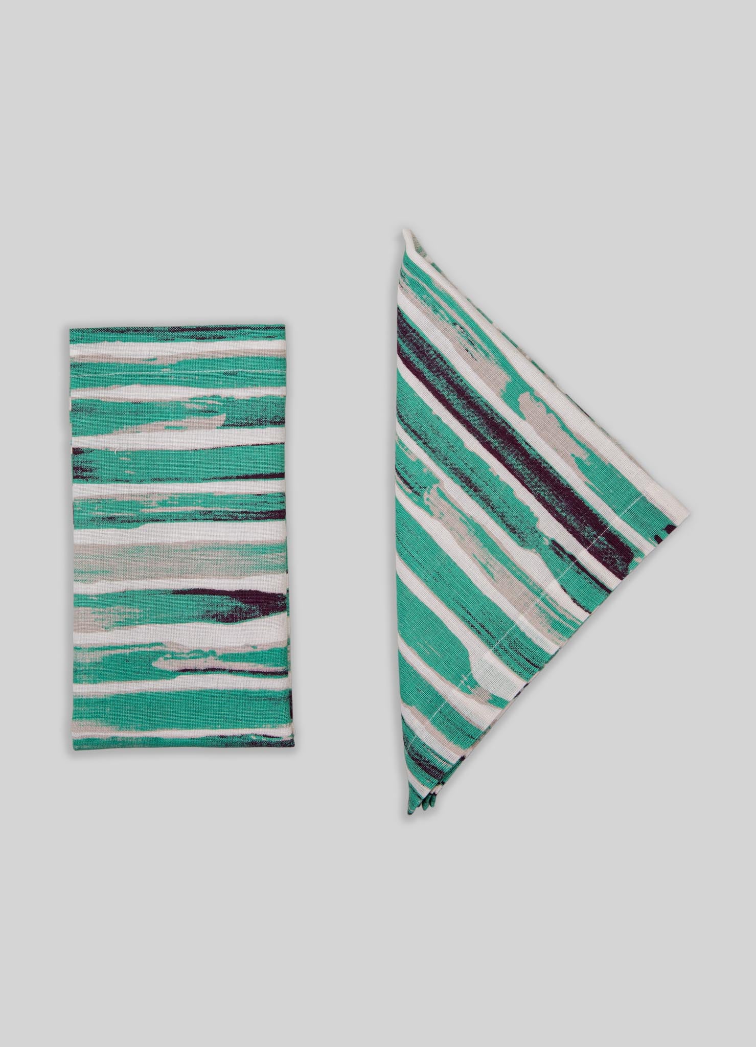 Striped textile accessories with abstract watercolor-like patterns in shades of teal, turquoise, white, and dark purple. The set includes a folded cloth and a napkin or placemat, crafted from woven fabric with a modern, artistic style.