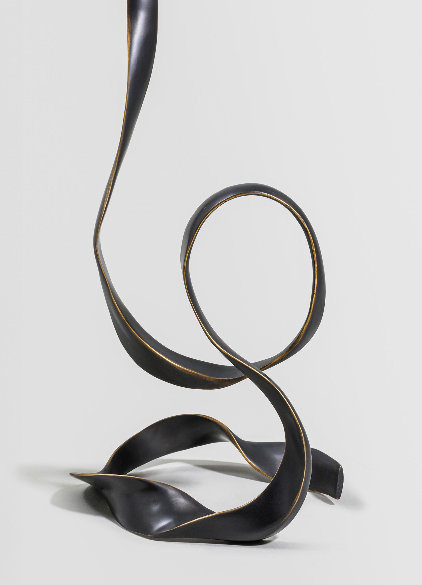 A sculptural metal lamp with flowing, curved lines and a matte black finish with gold accents. The design features organic, abstract shapes that evoke a contemporary, artistic style.