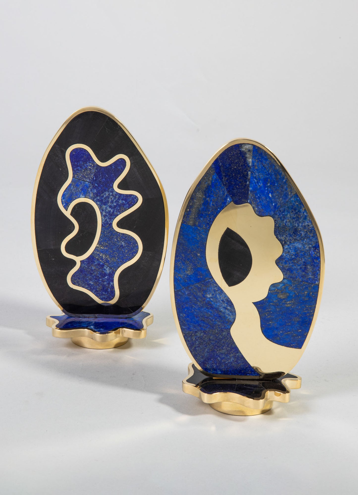 Decorative vases with abstract profiles, crafted from blue and black stone with gold-colored metal bases, featuring geometric and organic motifs in a modern style.