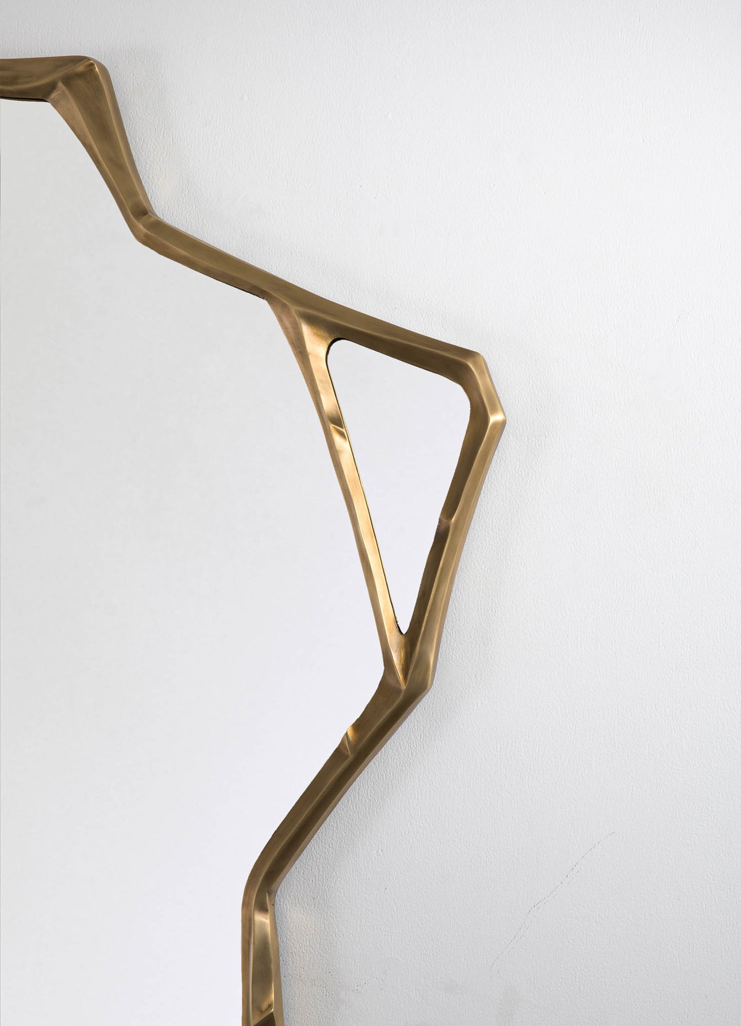 A modern brass handrail with geometric and angular design elements, mounted on a plain white wall.