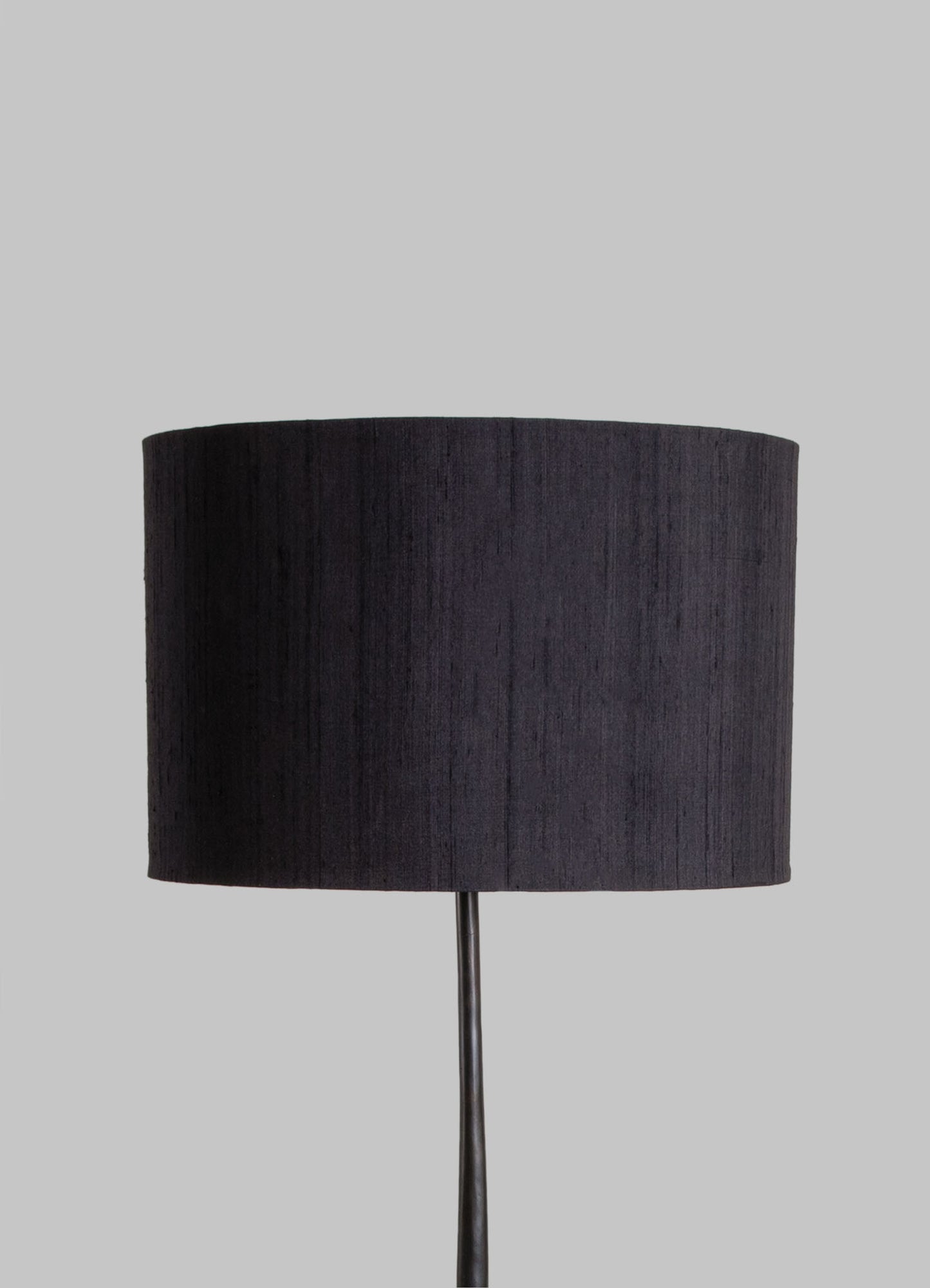 A table lamp with a black fabric drum shade and a slim metal stand, set against a neutral gray background.
