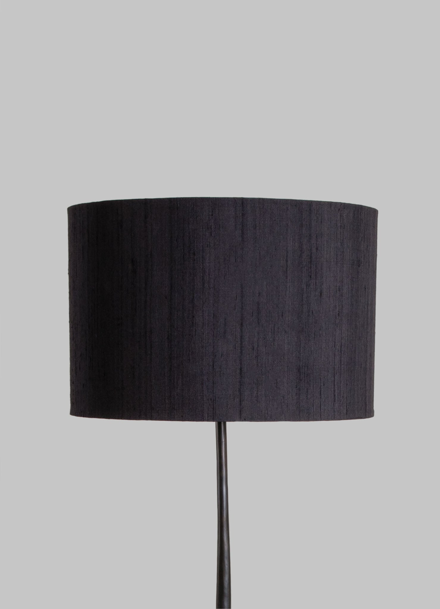 A table lamp with a black fabric drum shade and a slim metal stand, set against a neutral gray background.