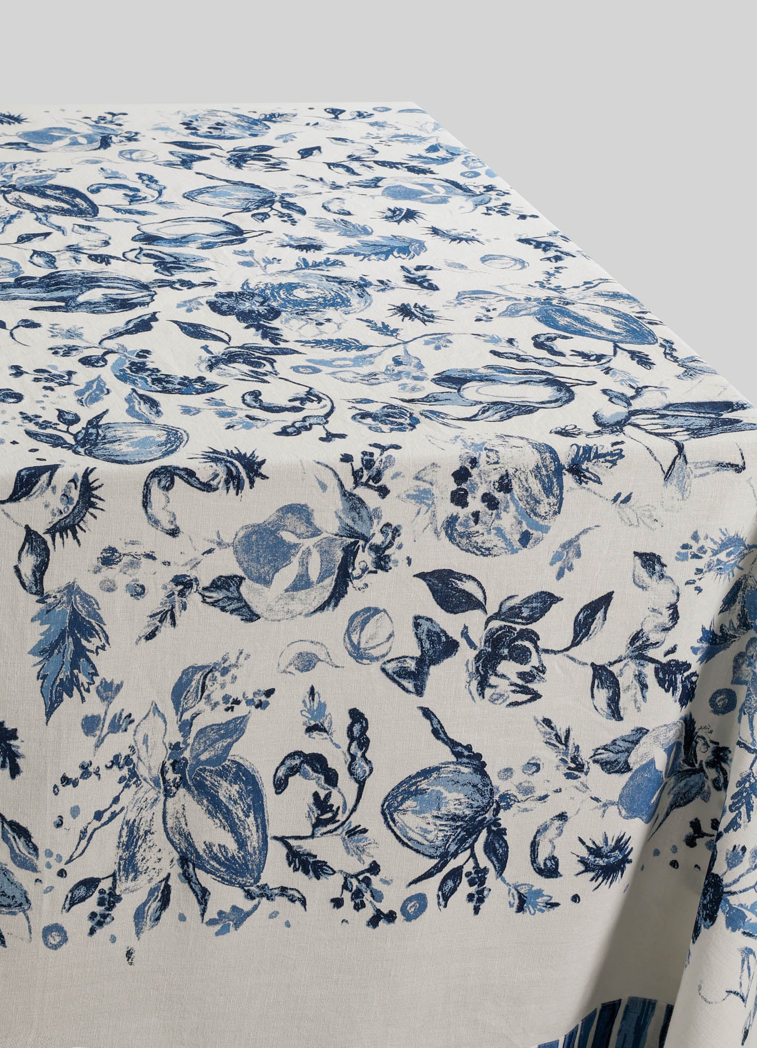Linen tablecloth with a botanical print in shades of blue on a white background, featuring floral and fruit motifs, with a smooth fabric surface and a contemporary style.