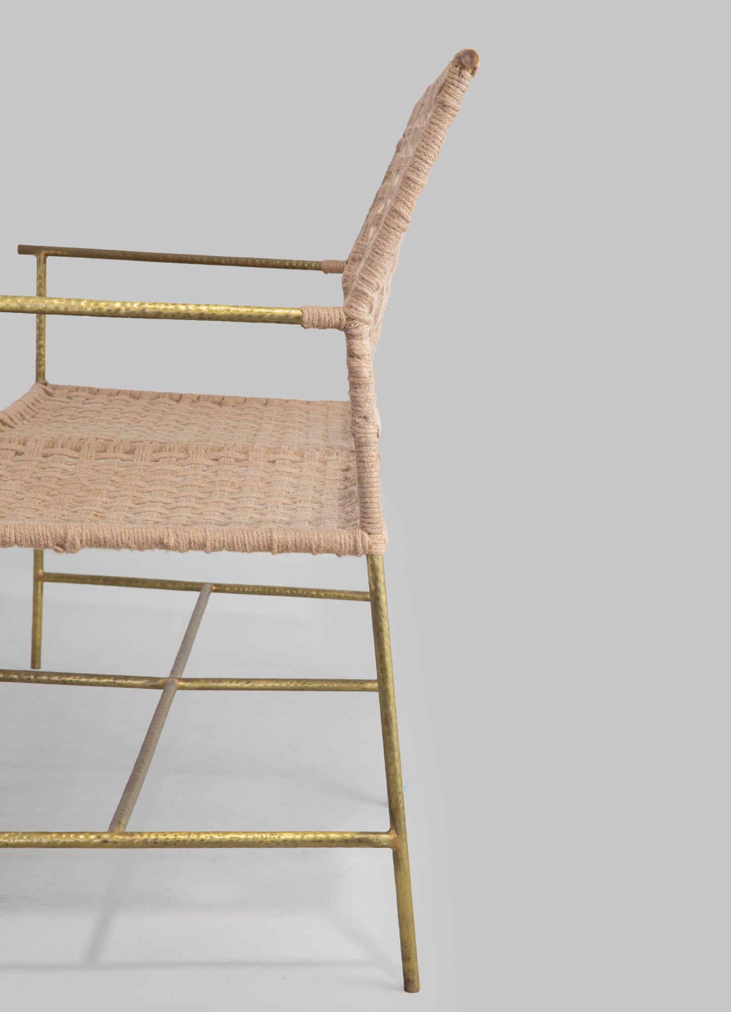 A chair with a frame made of textured brass or gold-toned metal, featuring a woven beige fabric seat and backrest. The overall style appears to be contemporary with a handcrafted and rustic aesthetic.