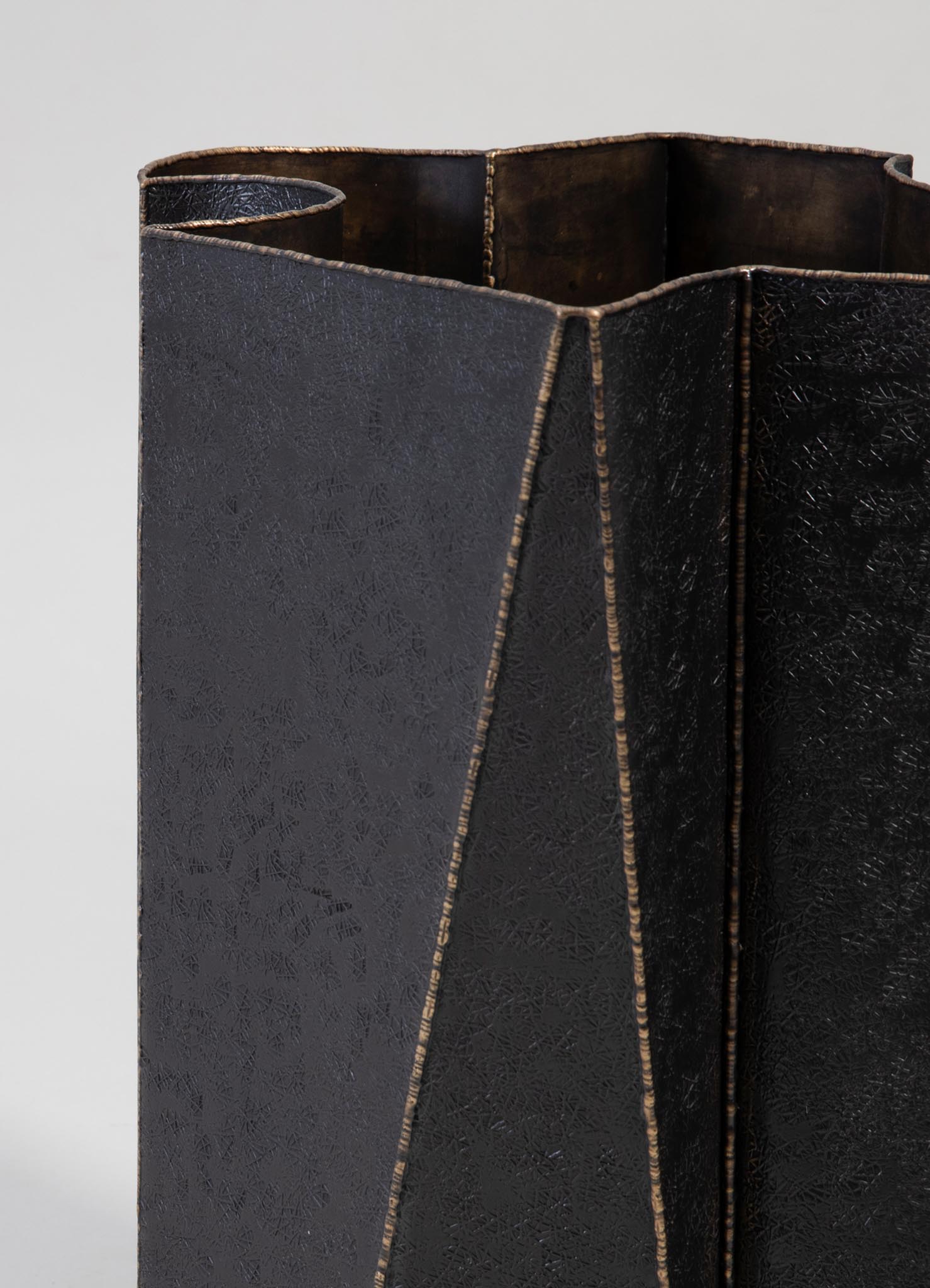 A black leather umbrella stand with angular, geometric design and subtle textured pattern, featuring gold-tone accents along the edges.