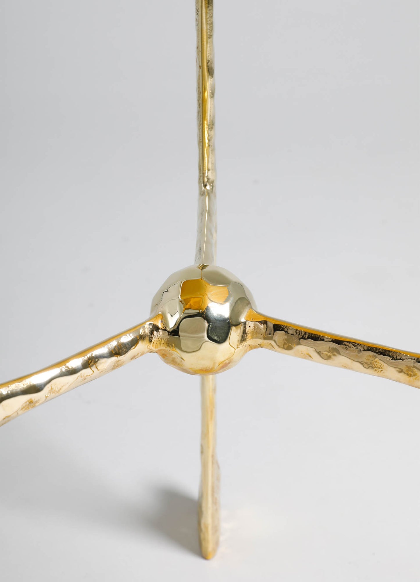 A close-up of a gold-toned metal sculpture with a spherical joint and three extendable arms, featuring a polished, reflective surface. The design has a modern and minimalist aesthetic, with a shiny metallic finish.