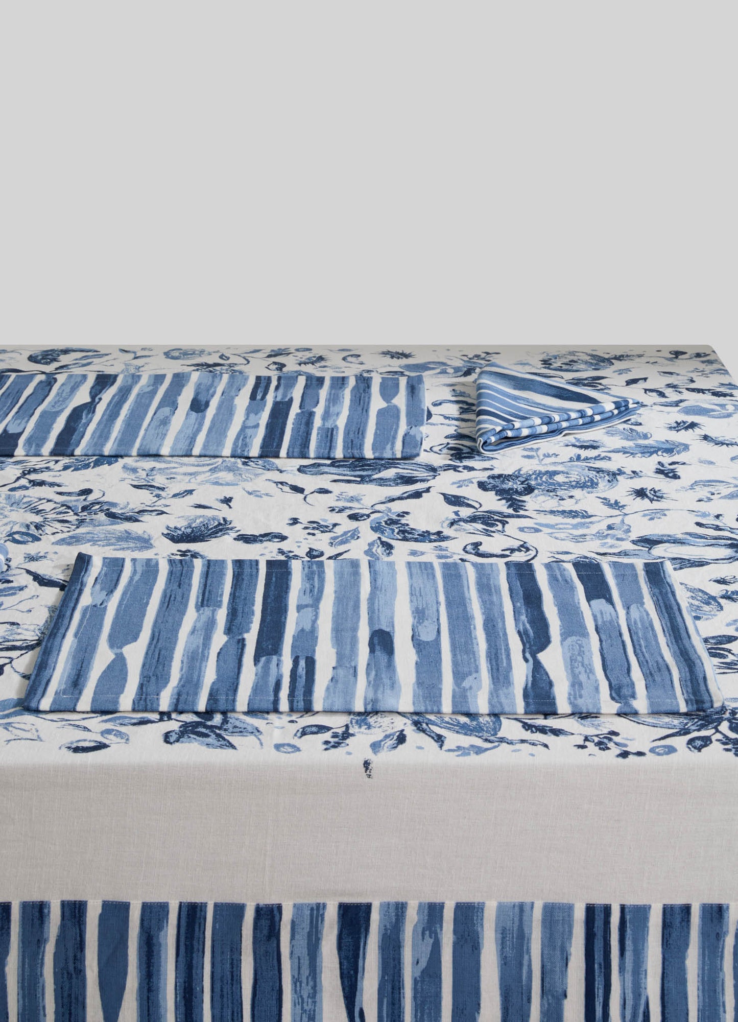 Cotton bed linen set with blue and white striped napkins and a floral print bedsheet featuring shades of blue and navy on a light background. The fabric combines casual and elegant styles with a maritime-inspired motif.