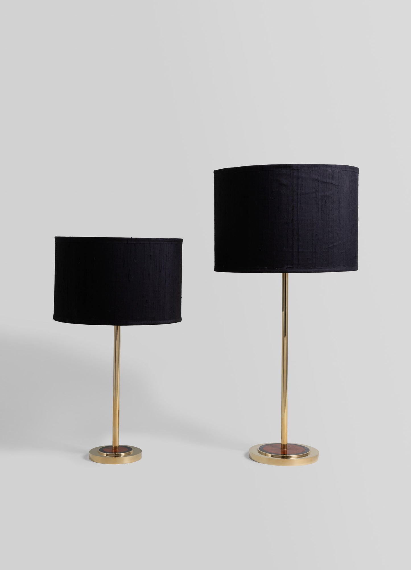 Pair of table lamps with black fabric drum shades and slender brass stems mounted on round brass bases, styled in a modern minimalistic design.