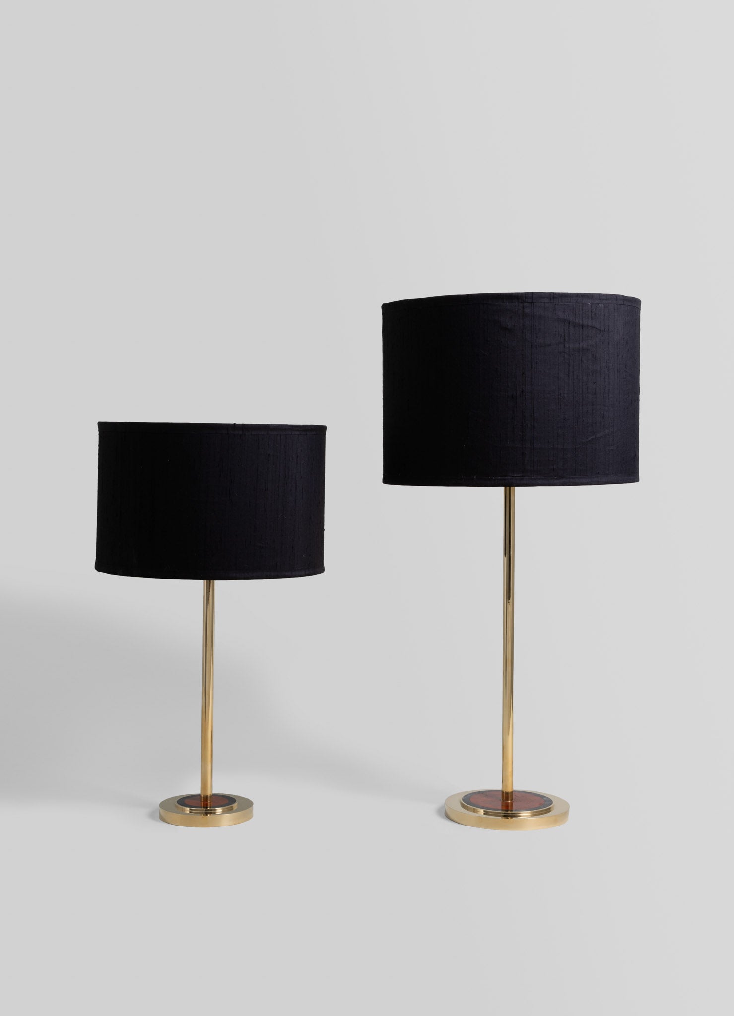 Pair of table lamps with black fabric drum shades and slender brass stems mounted on round brass bases, styled in a modern minimalistic design.