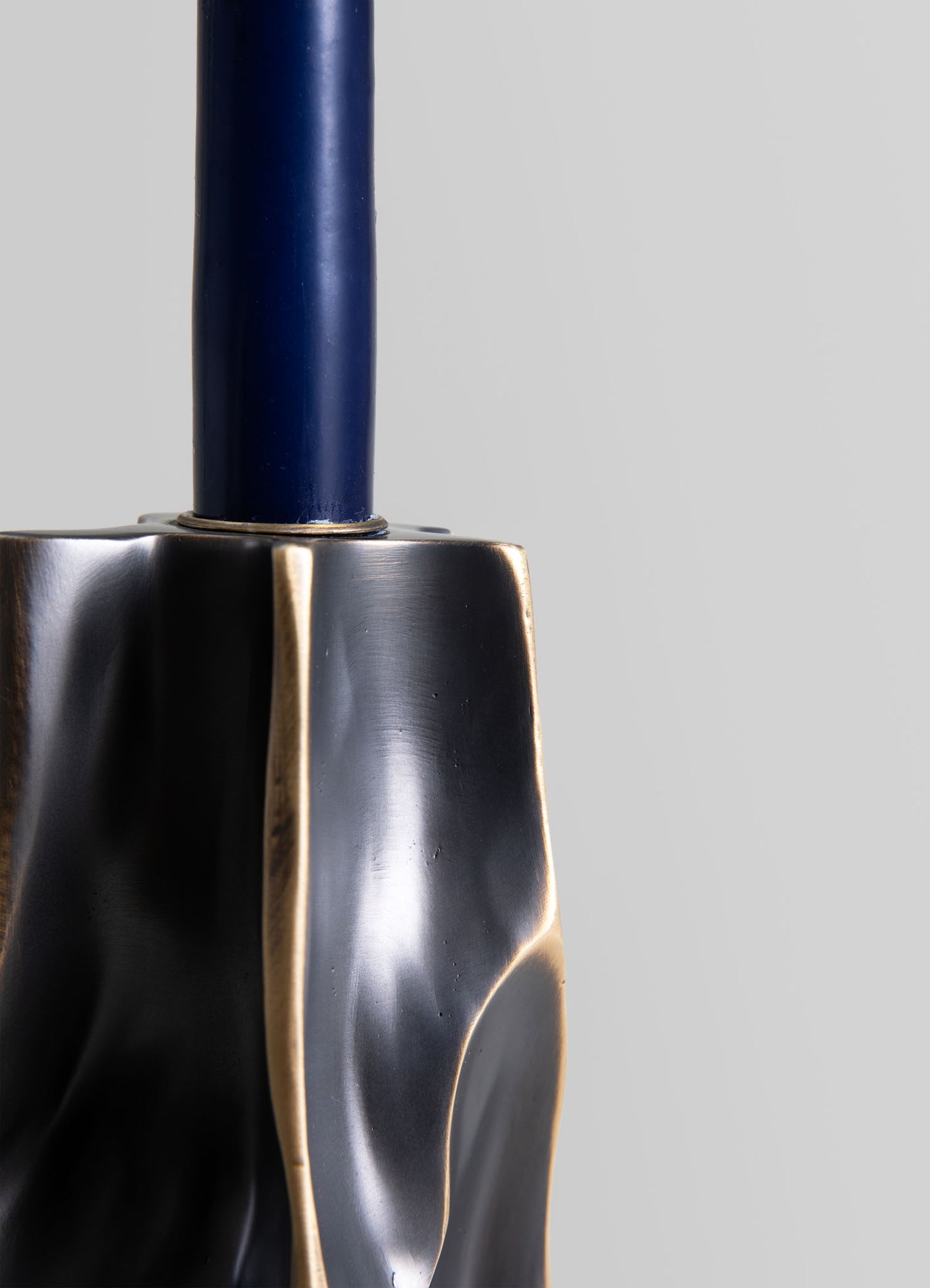 A metal sculpture with a black brushed finish and gold accents, featuring smooth, flowing curves and an elongated form, mounted on a blue cylindrical base. The piece has a contemporary, abstract style with polished surfaces and a sleek aesthetic.