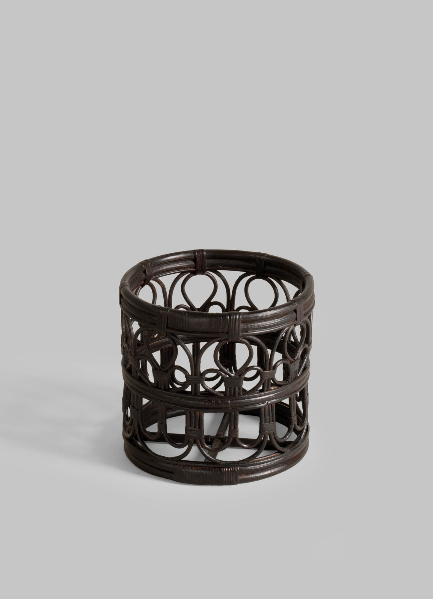 The VIYA Manipur Ice Bucket Small is a round, dark brown woven rattan piece with open circular patterns—ideal for storing barware or pairing with brass décor—shown against a light gray background.