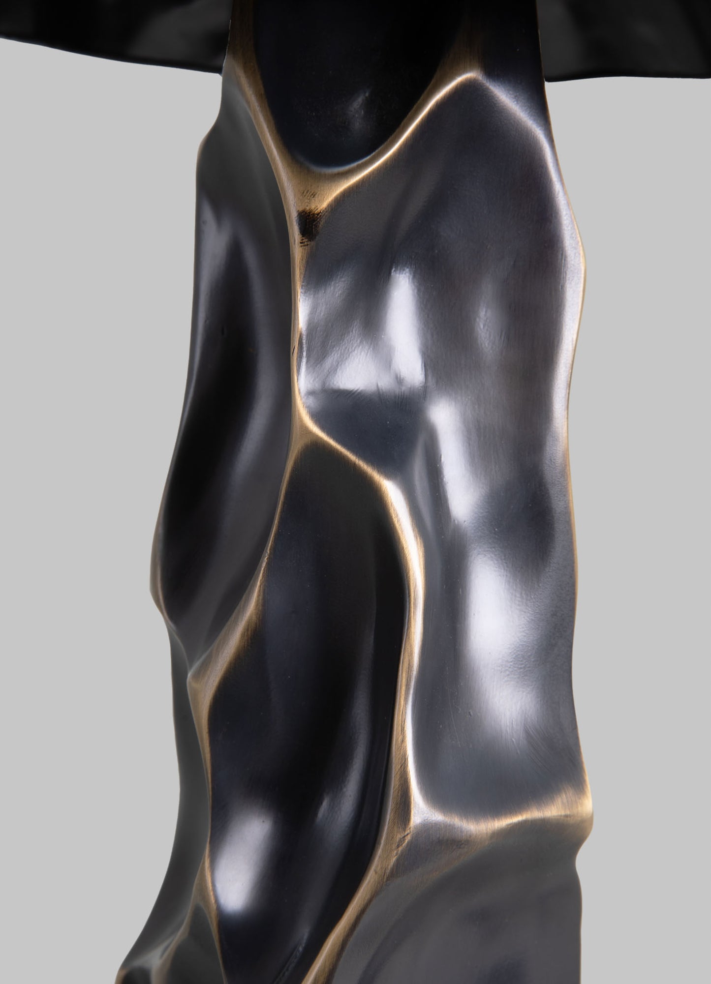 A metallic sculpture with an organic, abstract form, featuring smooth, flowing contours and a polished surface with black and gold tones.