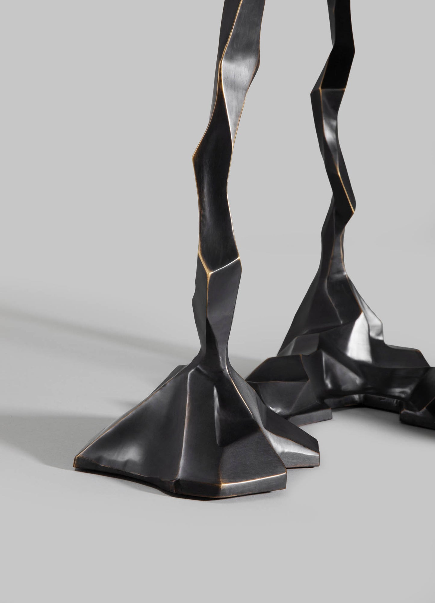 Two black metal sculpture bases with angular, faceted design and a matte finish, featuring gold-toned edges and irregular geometric shapes.