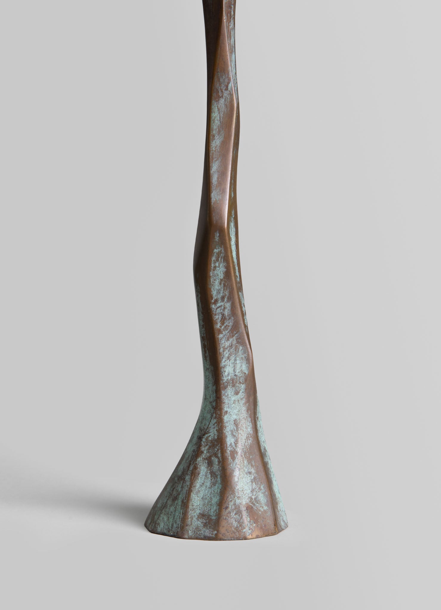 A sculptural table leg made of metal with a twisted, organic shape and a distressed finish in bronze and turquoise tones, contributing to a rustic and artistic style.