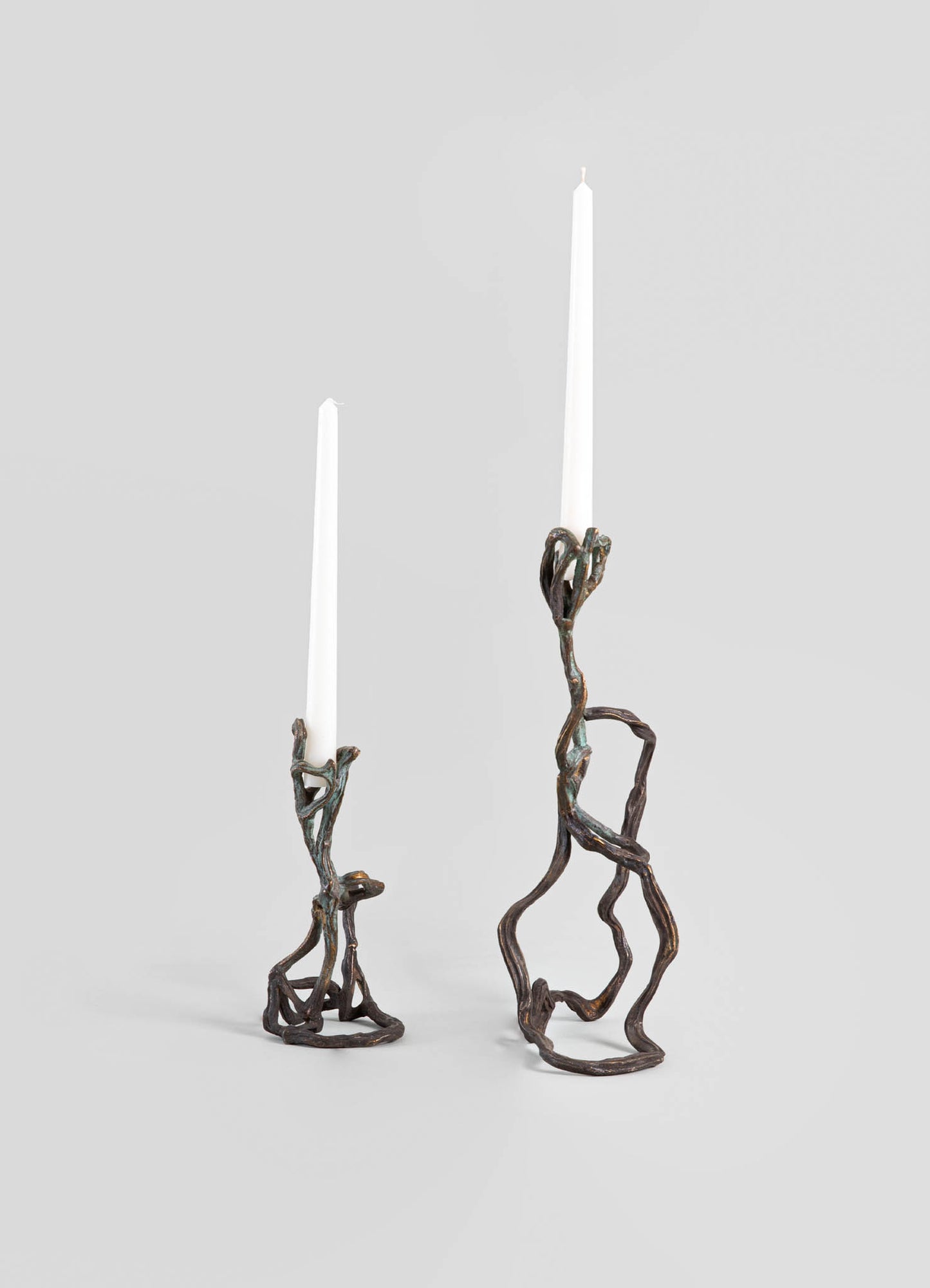 Metal candlestick holders with a twisted, organic design in dark bronze finish, each holding a tall white taper candle.