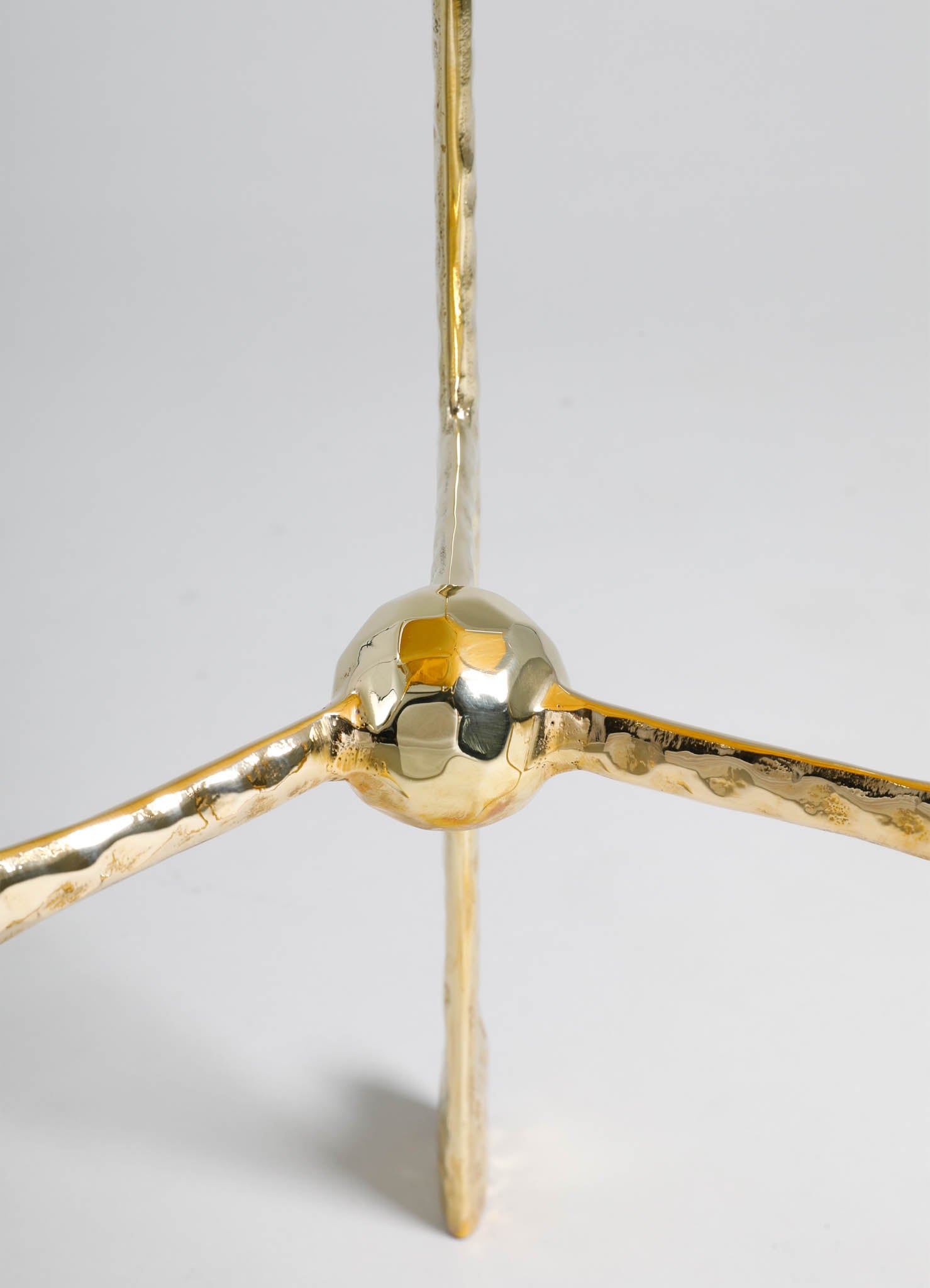 A metallic gold and brass sculpture with a spherical joint connecting three elongated, textured rods. The sculpture has a contemporary design with a polished, reflective surface.