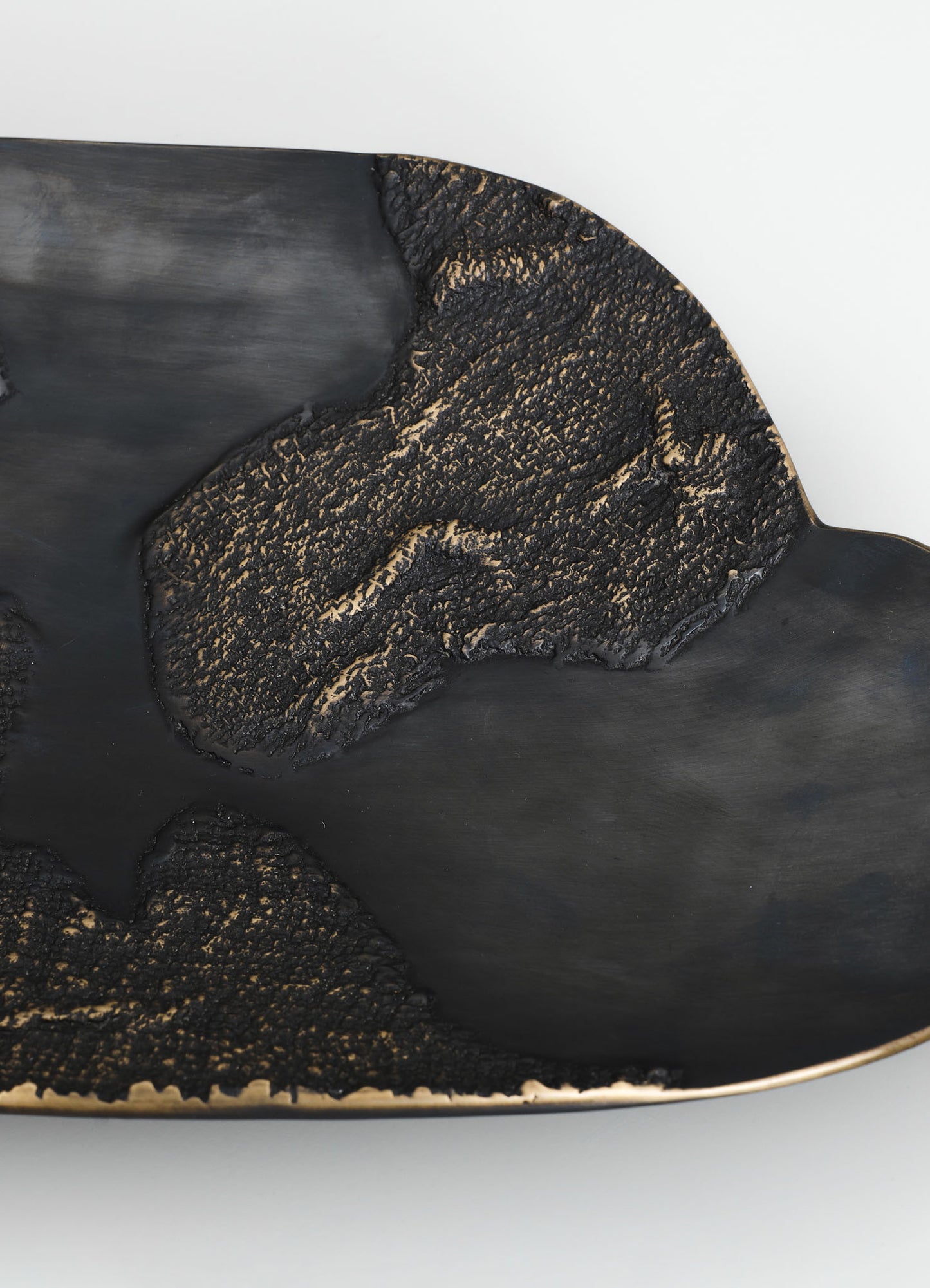 A decorative black ceramic tray with textured, gold-accented floral motifs and a smooth matte finish, featuring an irregular oval shape.