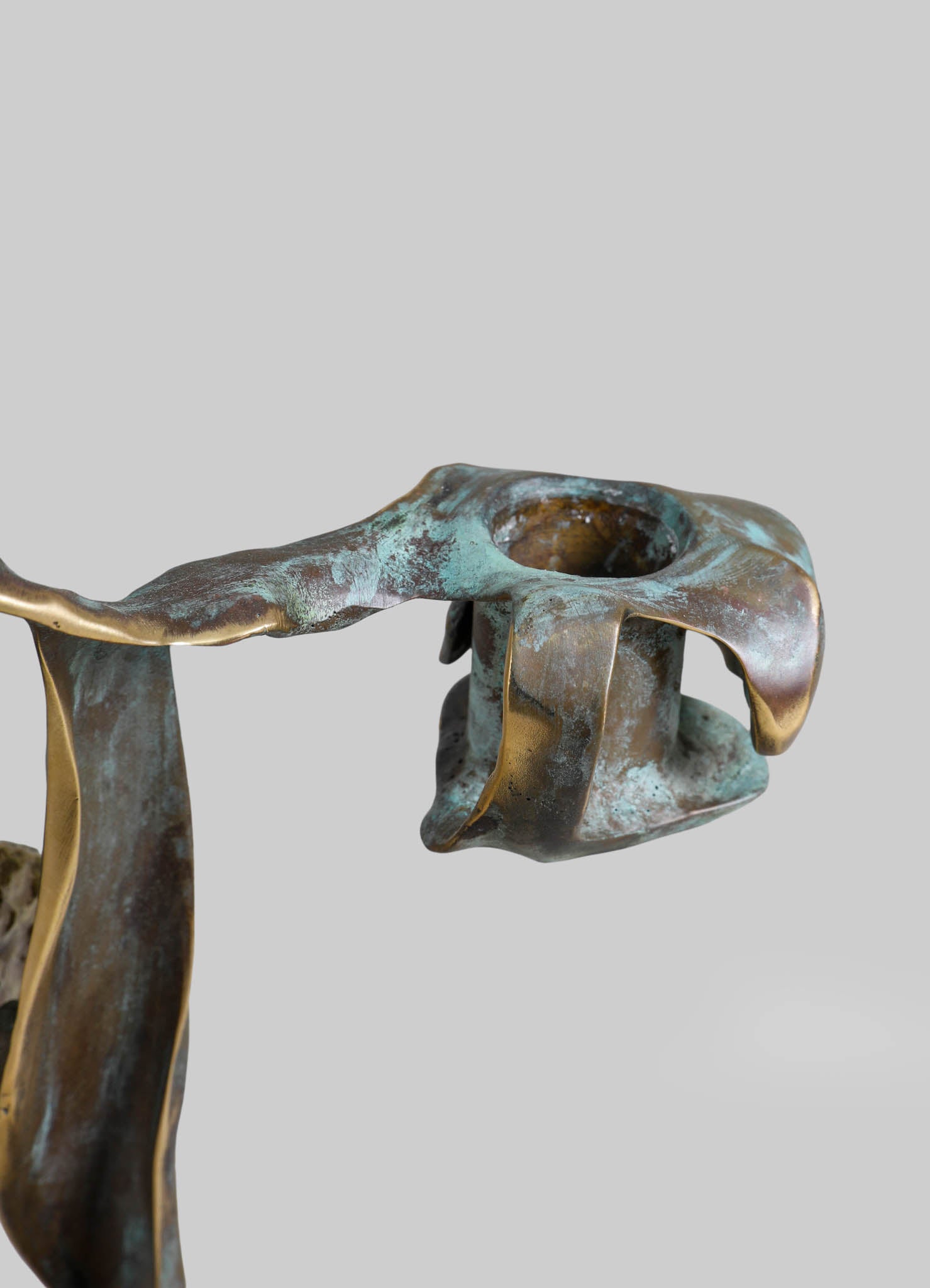 Patinated bronze candle holder with an organic, sculptural shape and metallic finish, featuring flowing, irregular edges reminiscent of natural forms.