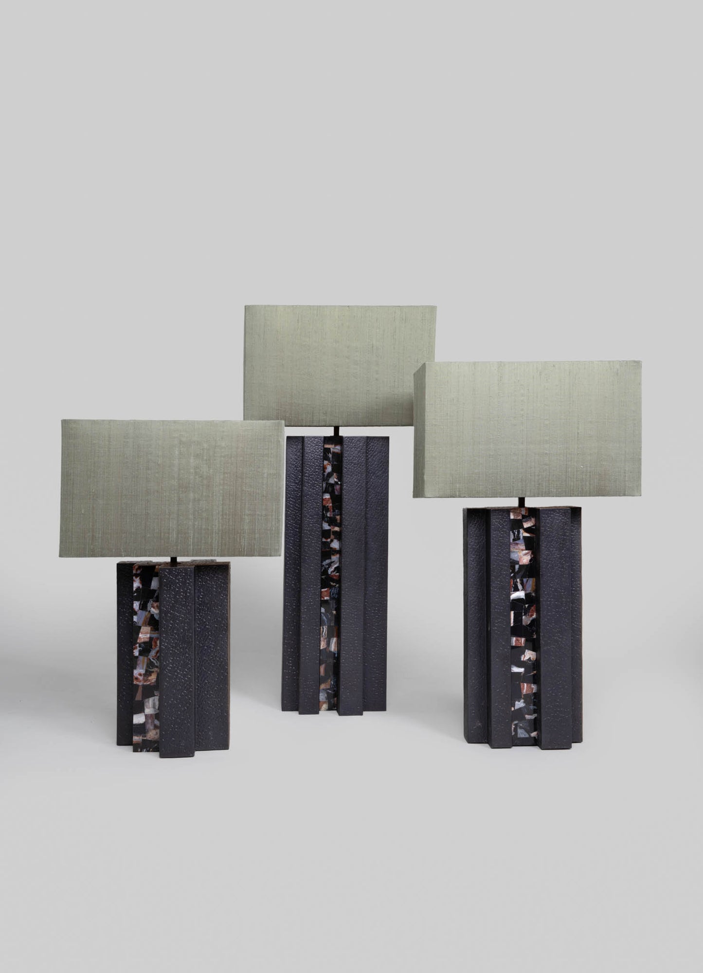 Three table lamps with rectangular fabric shades in light beige and bases made of textured black material with multicolored marbled accents. The lamps have a modern, geometric style with a rustic yet contemporary aesthetic.