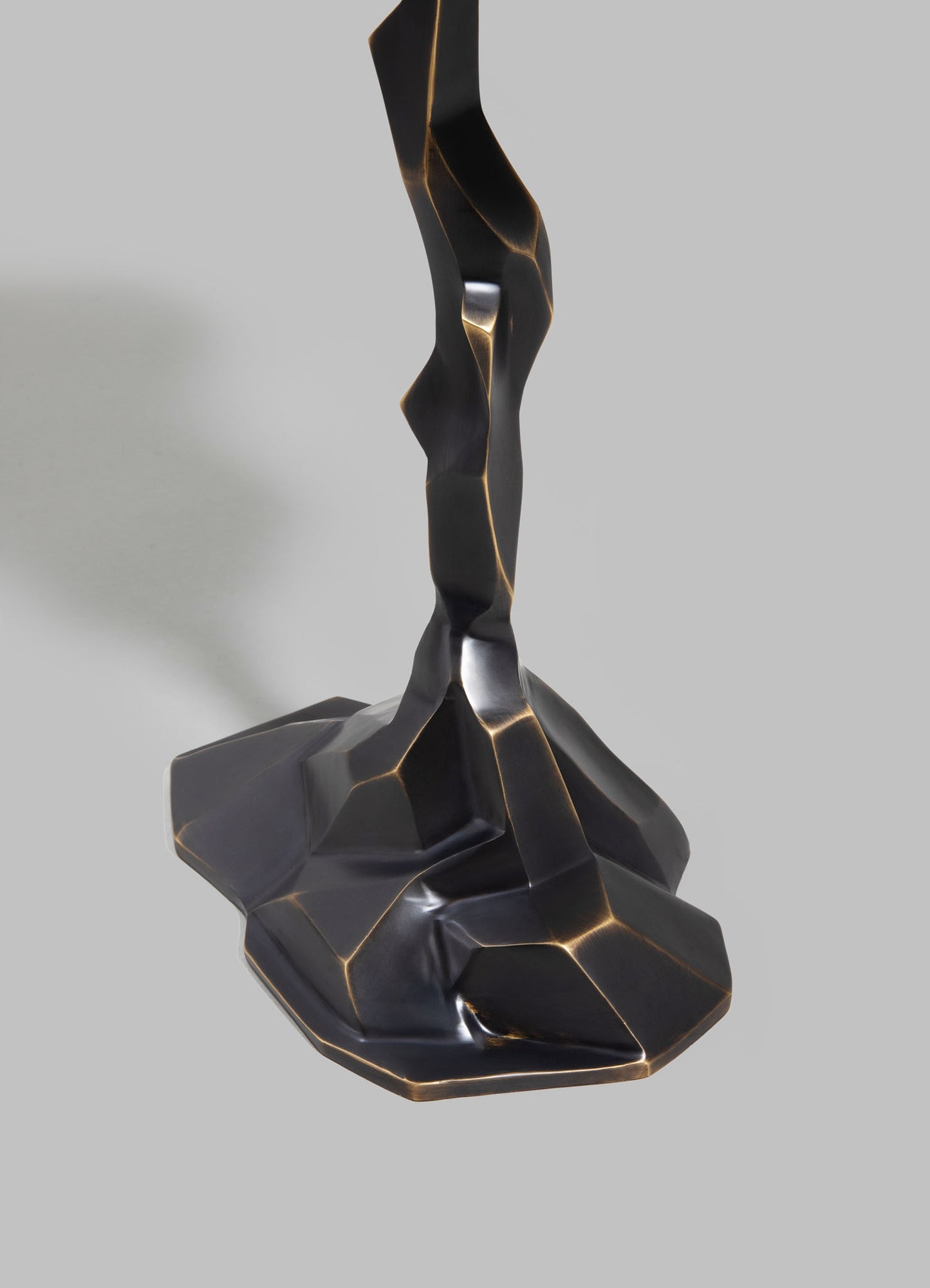 A sculptural table lamp with a twisted, organic form in black metal with gold accents, featuring a contemporary and abstract design. The base is broad and irregular, supporting a slender, winding stem that tapers upward.