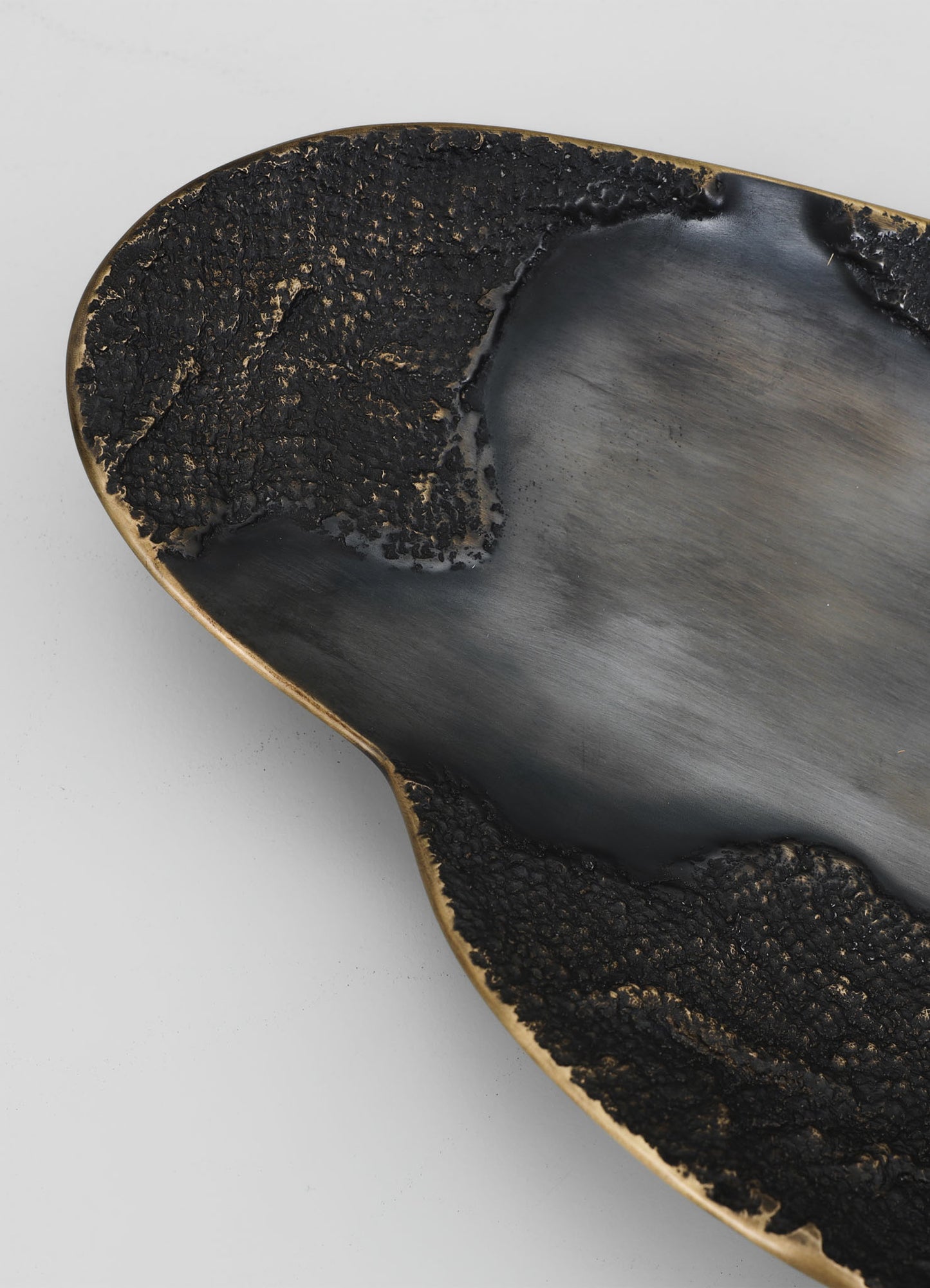 A ceramic or metal bowl with a matte black interior and a textured, burnt-looking black and gold exterior finish, featuring an organic, asymmetrical shape.