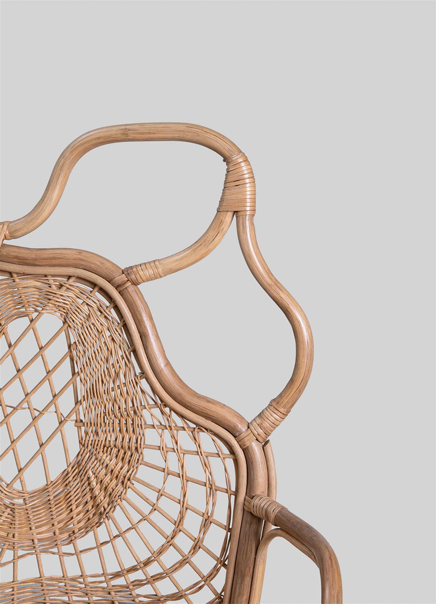 Wicker chair with a circular woven backrest, natural rattan frame, and curved armrests, showcasing handcrafted rustic style and earthy tones.