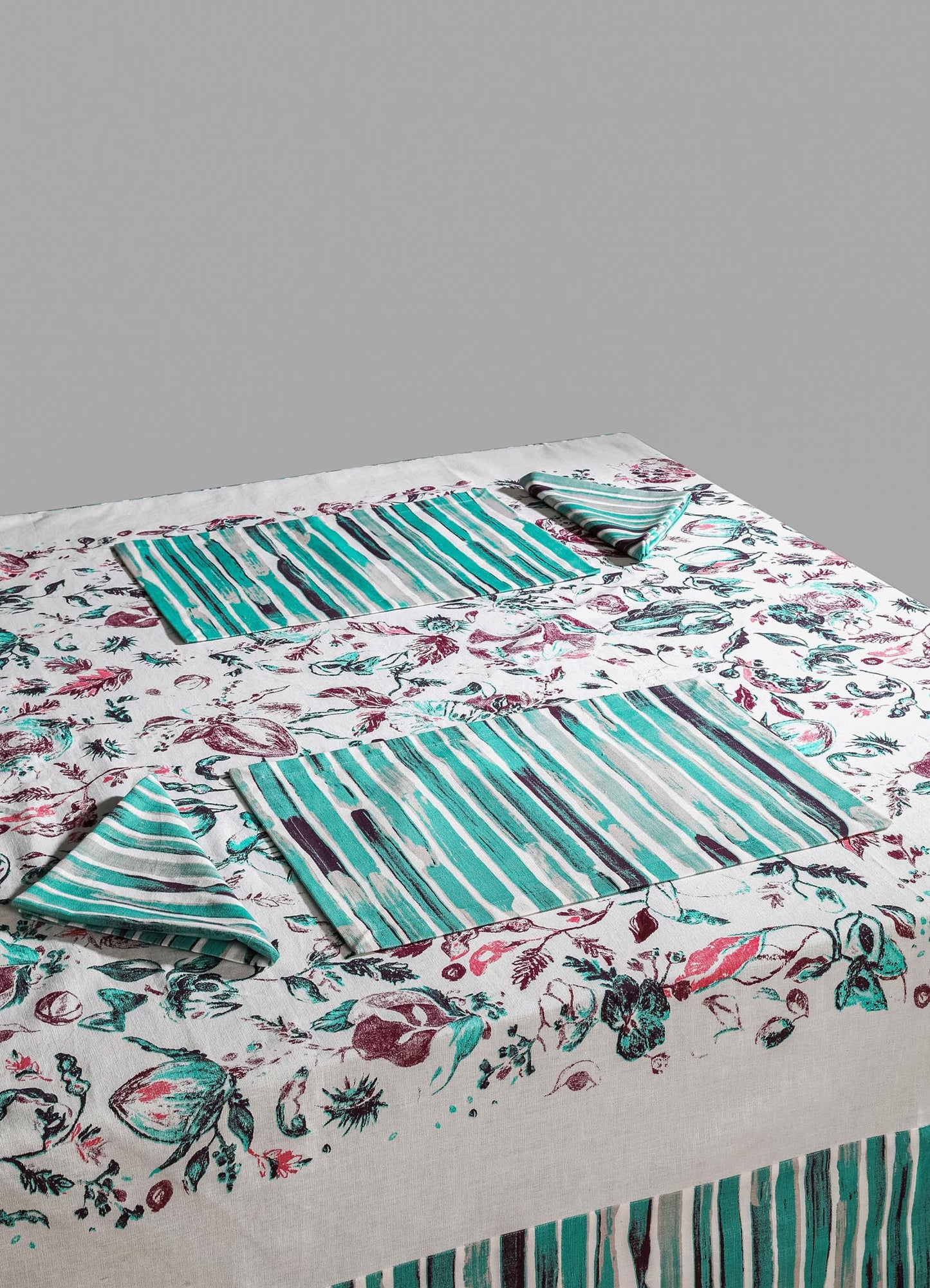 Cotton tablecloth with a floral and botanical print in shades of burgundy, teal, and black, accented by matching striped placemats and napkins in turquoise, white, and black. The design combines a rustic and contemporary style with a vibrant, pattern-rich aesthetic.