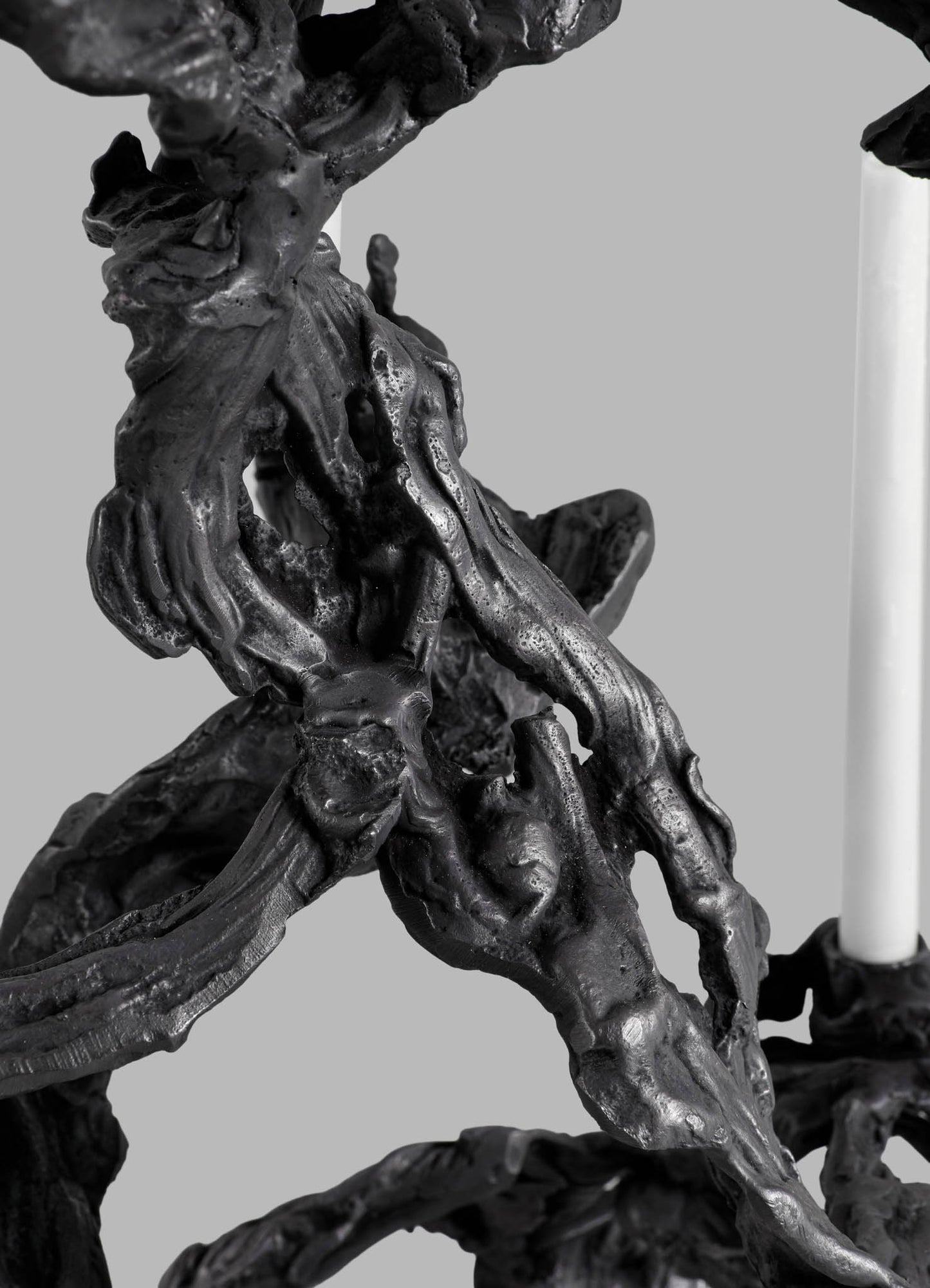 A close-up of a black decorative sculpture with a textured, organic form resembling intertwined natural elements, made from a glossy material. The background is neutral gray, highlighting the intricate, flowing shapes of the piece.