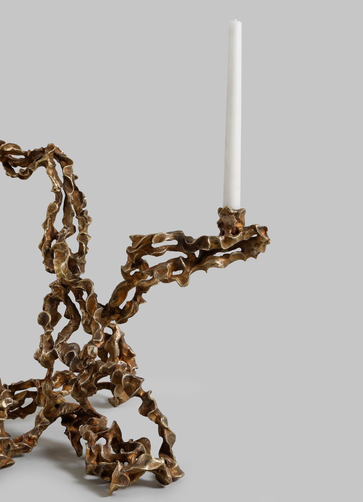 Brass candle holder with an organic, sculptural design featuring twisted, irregular shapes and a matte finish, holding a single white taper candle.