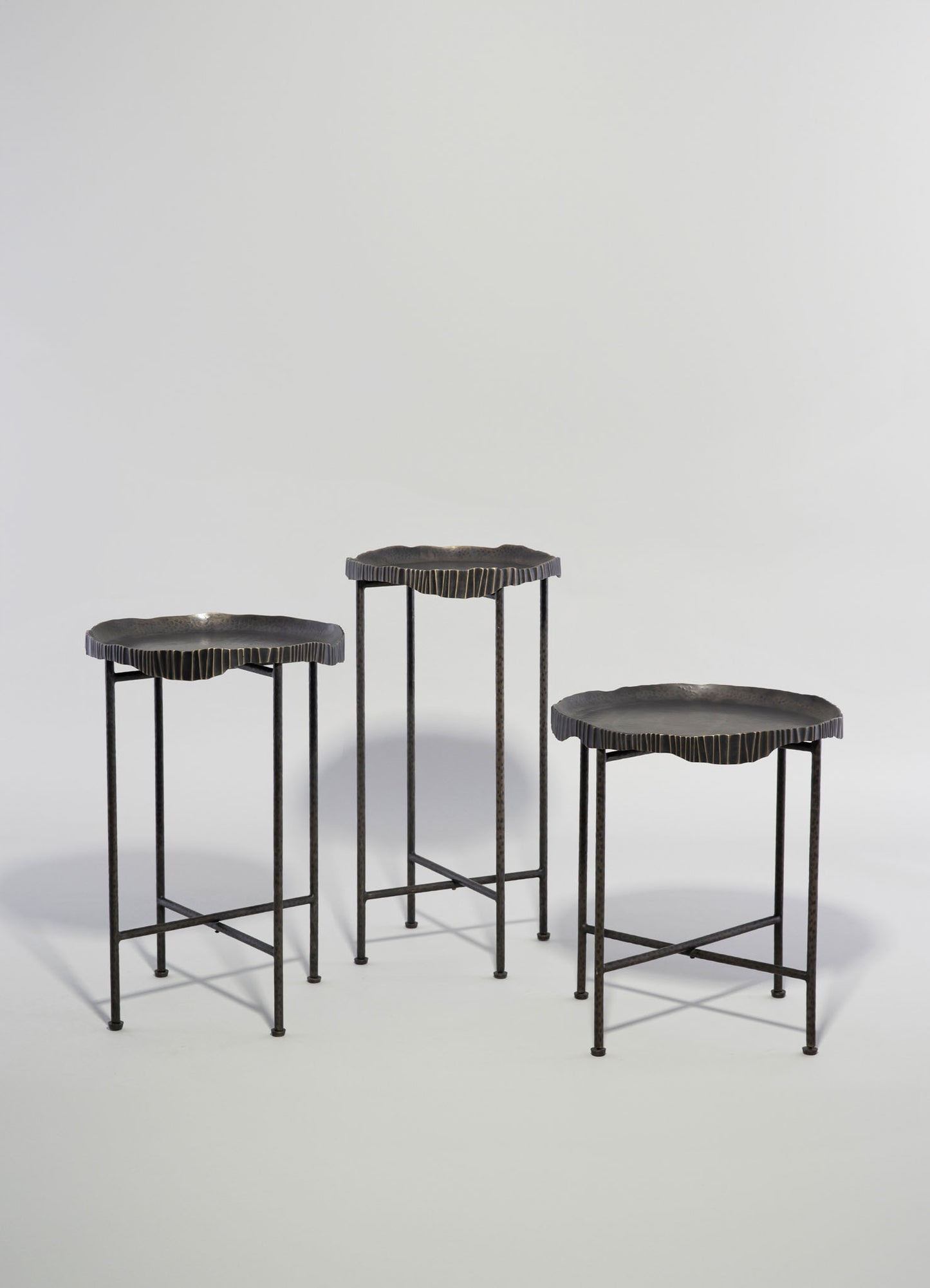 Set of three metal side tables with irregular, scalloped edges on slender black metal legs, featuring a matte black finish. The tables have a minimalist and contemporary style.