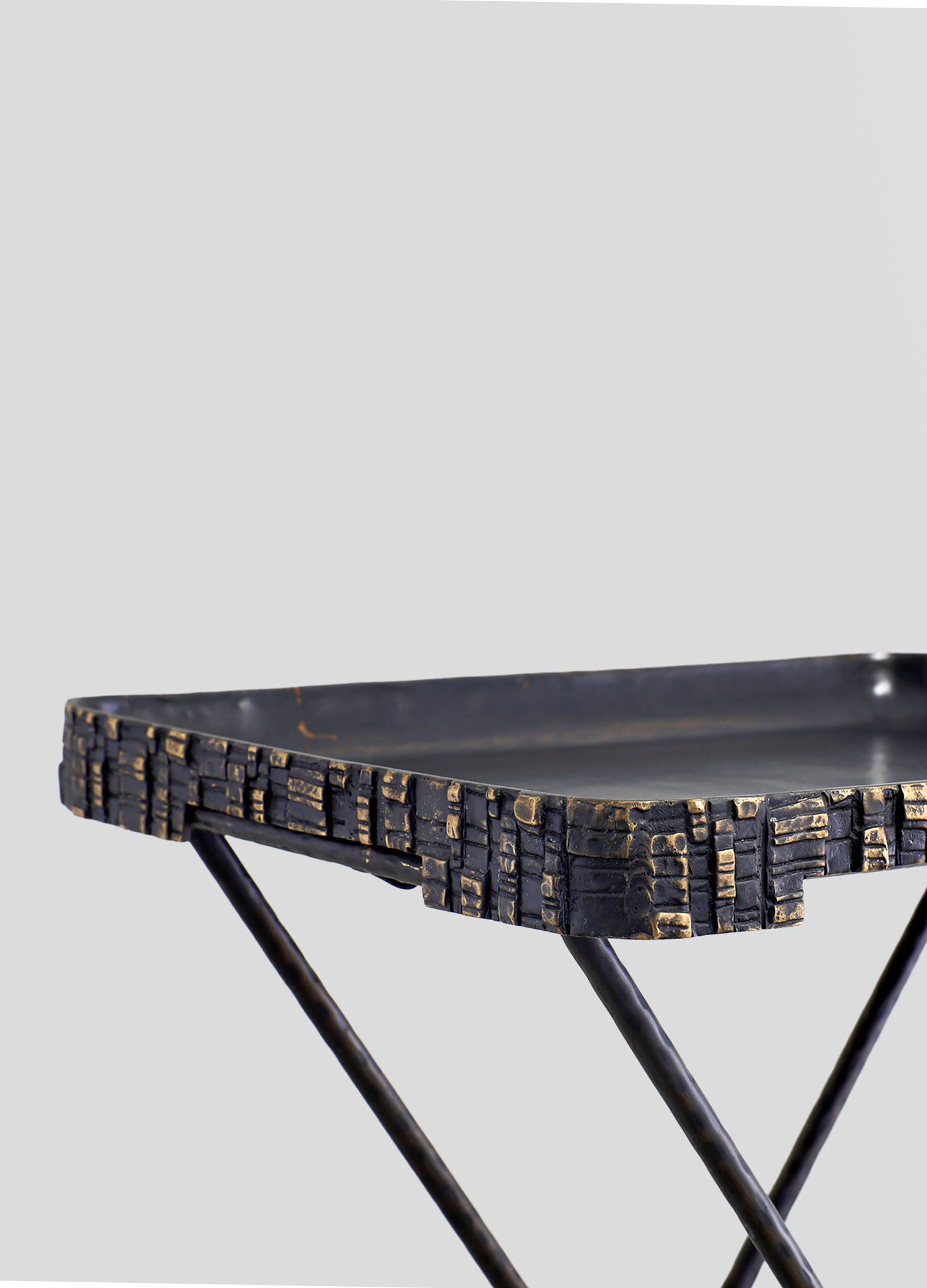 Black and gold textured metal tray with a geometric pattern, supported by slender black metal legs.