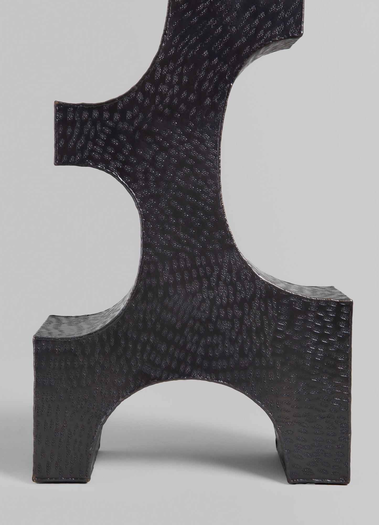 A black ceramic decorative sculpture with a textured,Scale-like surface pattern and geometric form, featuring curved edges and an abstract design.