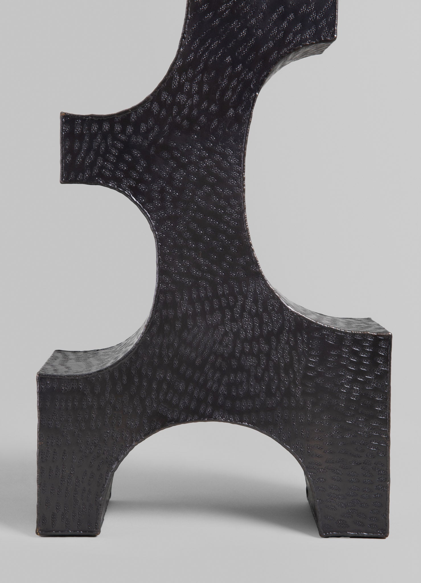 A black ceramic decorative sculpture with a textured,Scale-like surface pattern and geometric form, featuring curved edges and an abstract design.