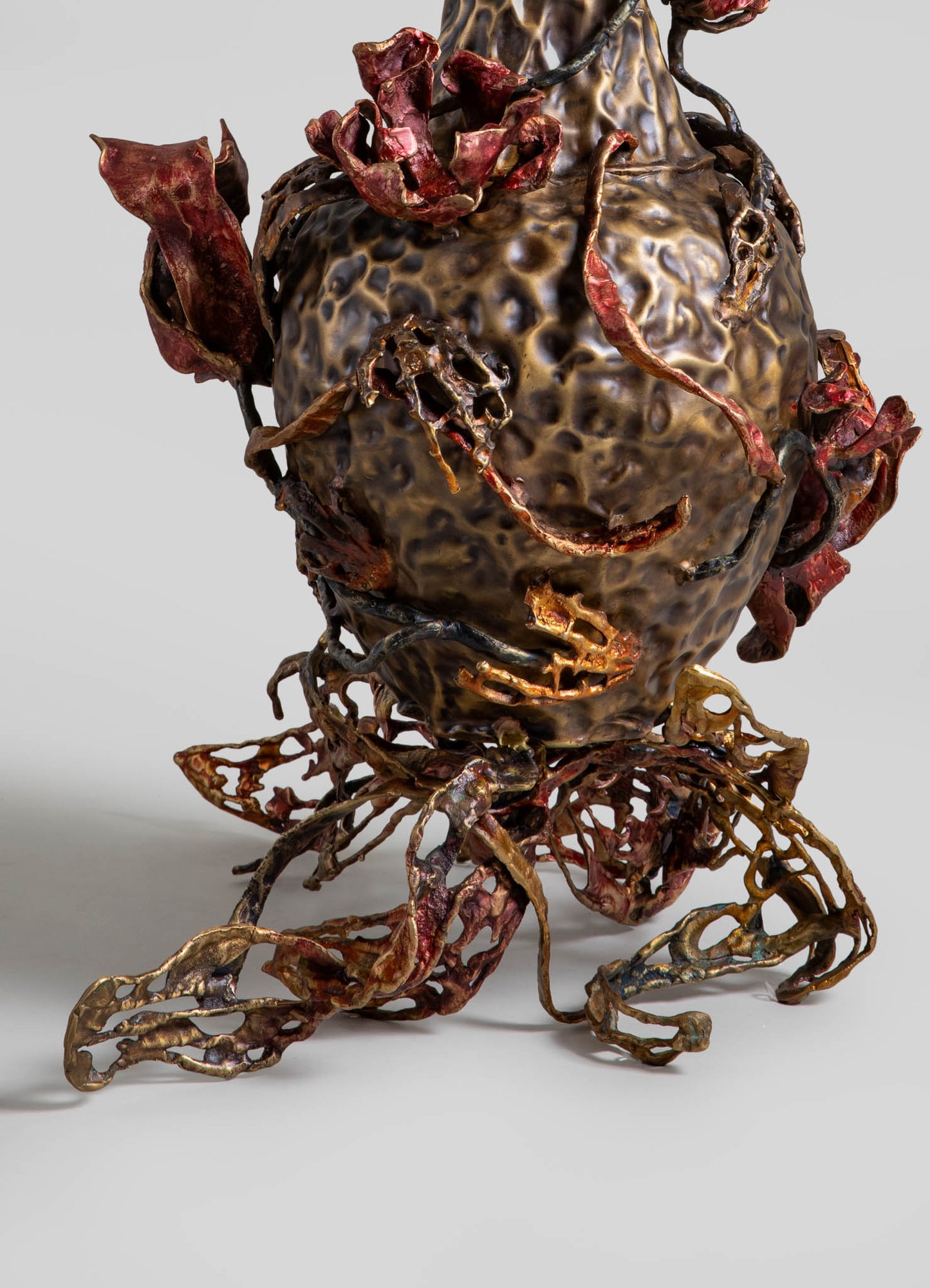 A sculptural decorative piece featuring a textured, metallic-finished surface with organic, twisting forms in bronze tones, adorned with reddish-brown accents that resemble dried flowers or floral motifs.