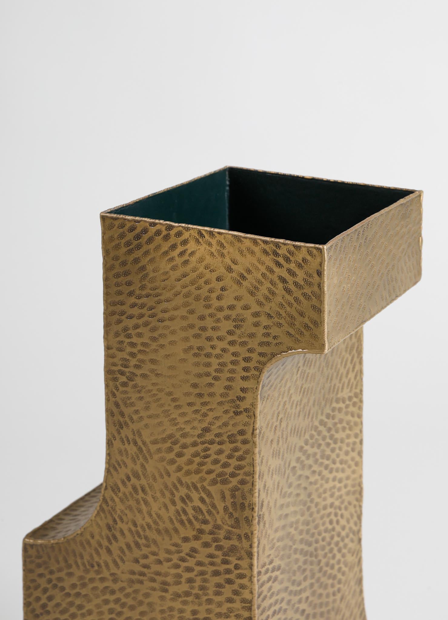 A textured gold-colored vase with a hammered metal finish featuring a curved opening at the top and a contrasting dark interior, designed in a contemporary style.
